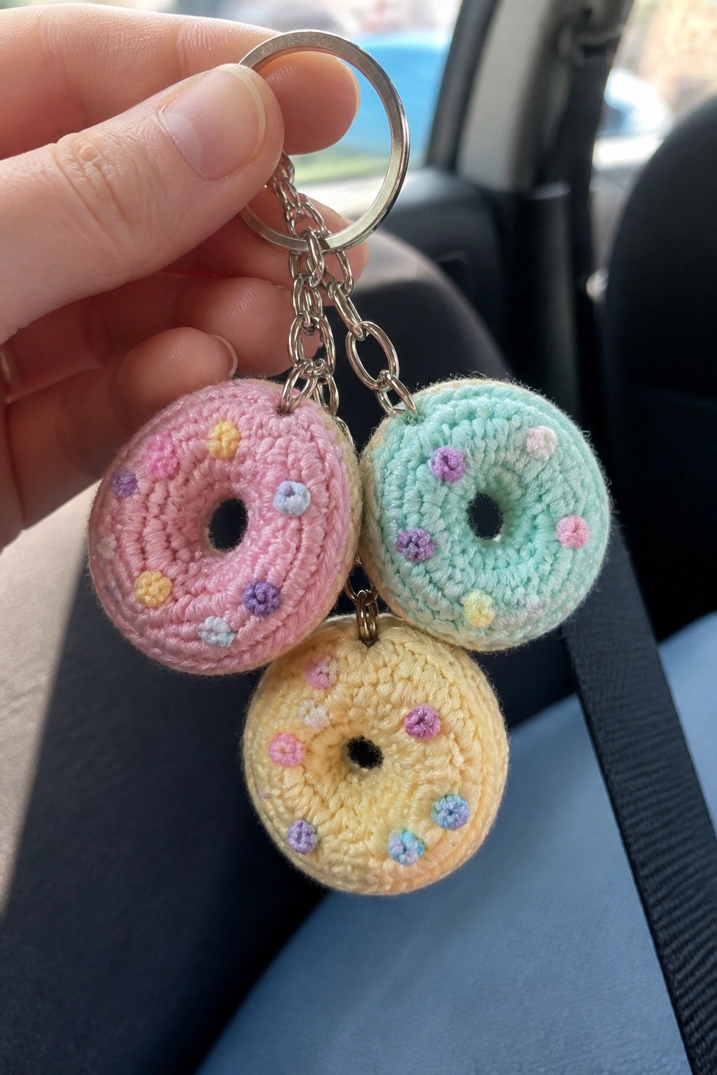 Hand holding keychain with three pastel crocheted donut charms in pink, mint, and yellow.