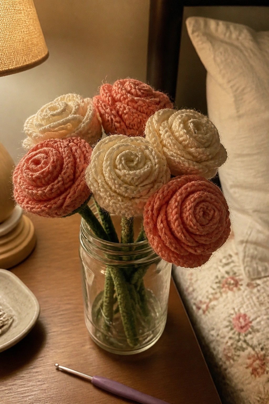 Crocheted peach and cream roses in a glass jar beside a crochet hook on a table