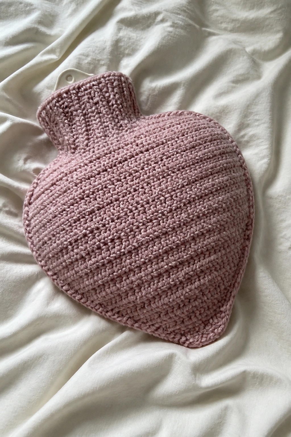 Pink knitted heart-shaped hot water bottle cover on white wrinkled fabric.