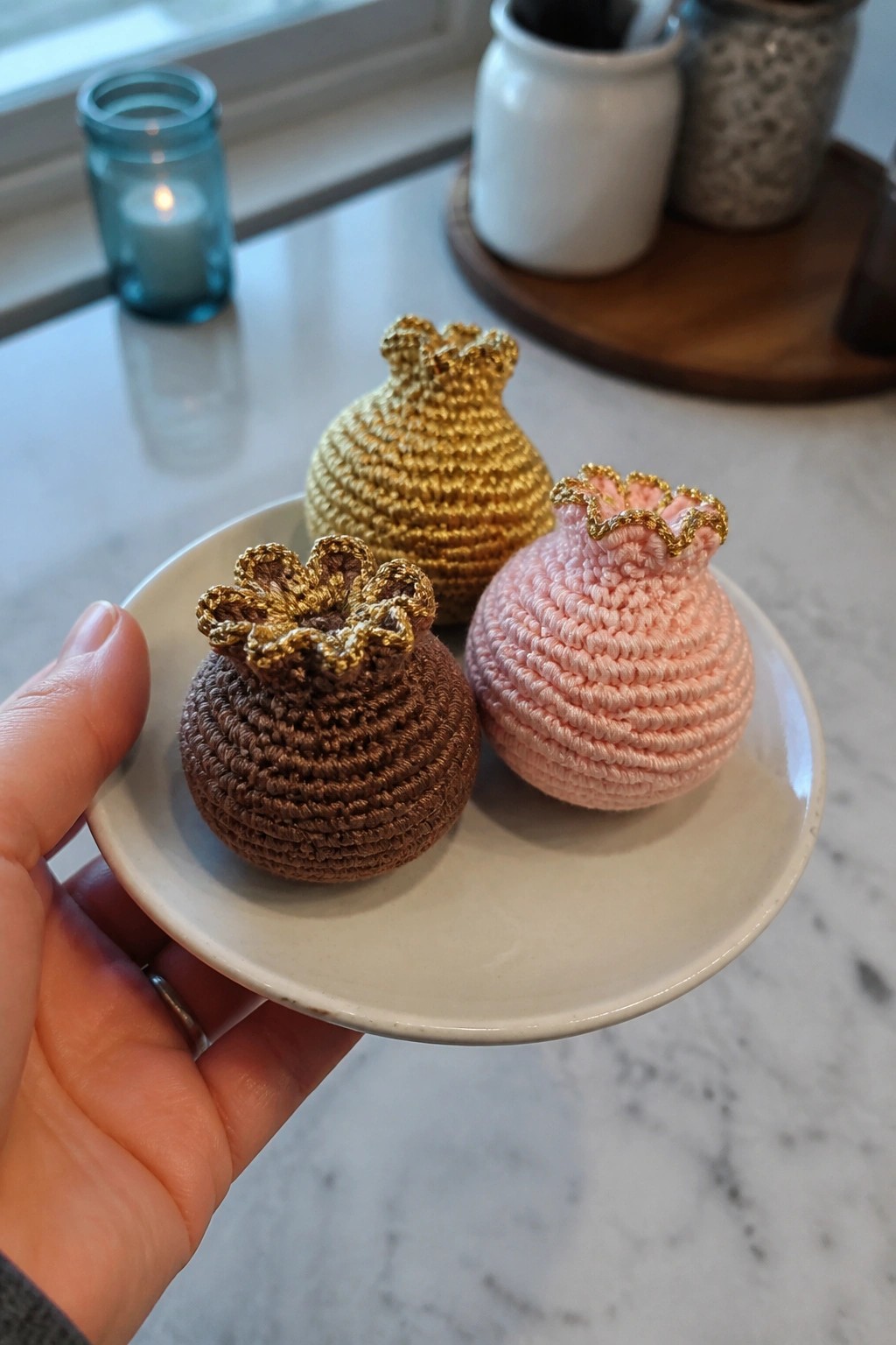Hand holding plate with three crocheted pouches in brown, gold, and pink