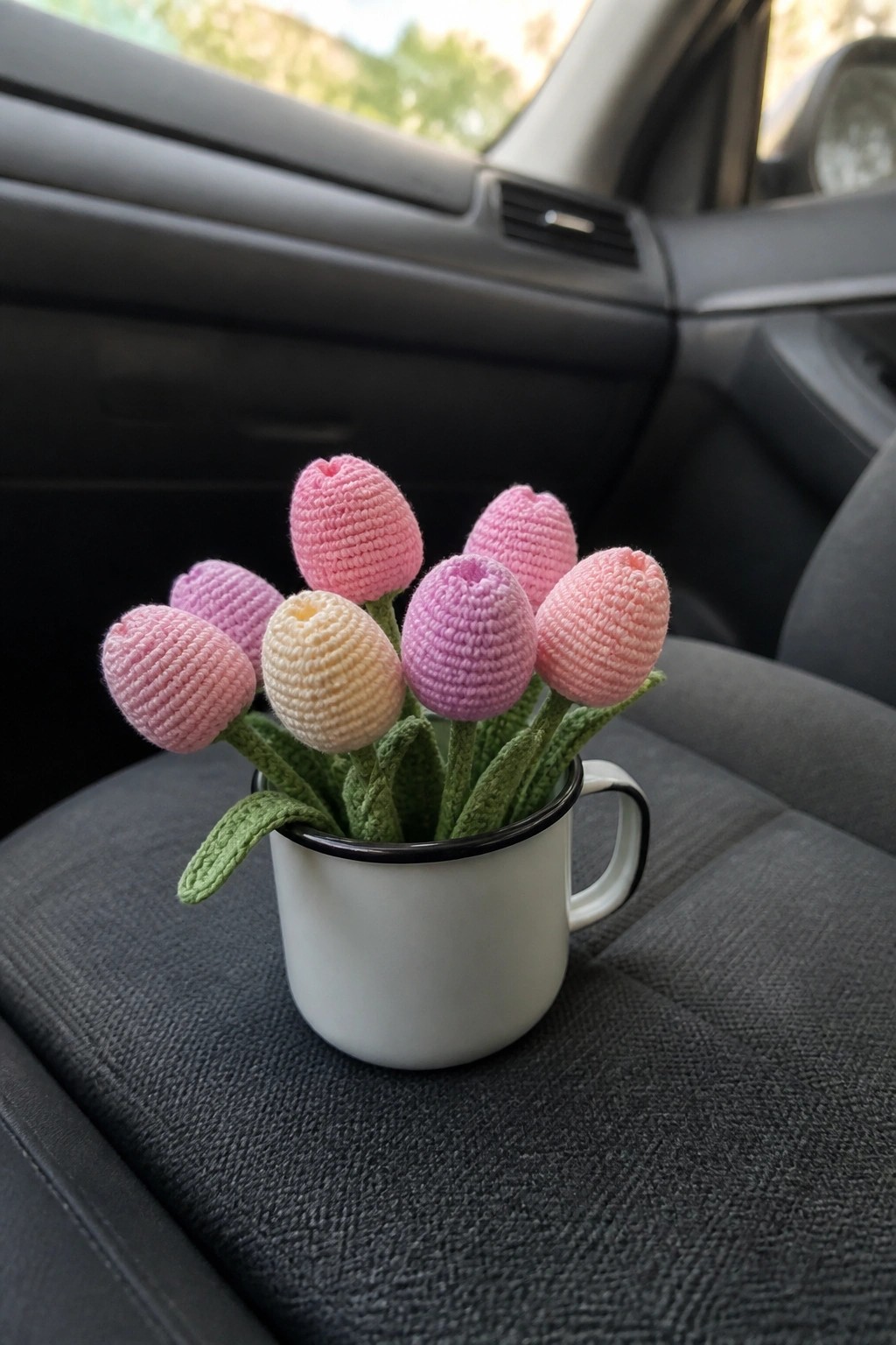 Pink and yellow crocheted tulips in a white mug on a car seat