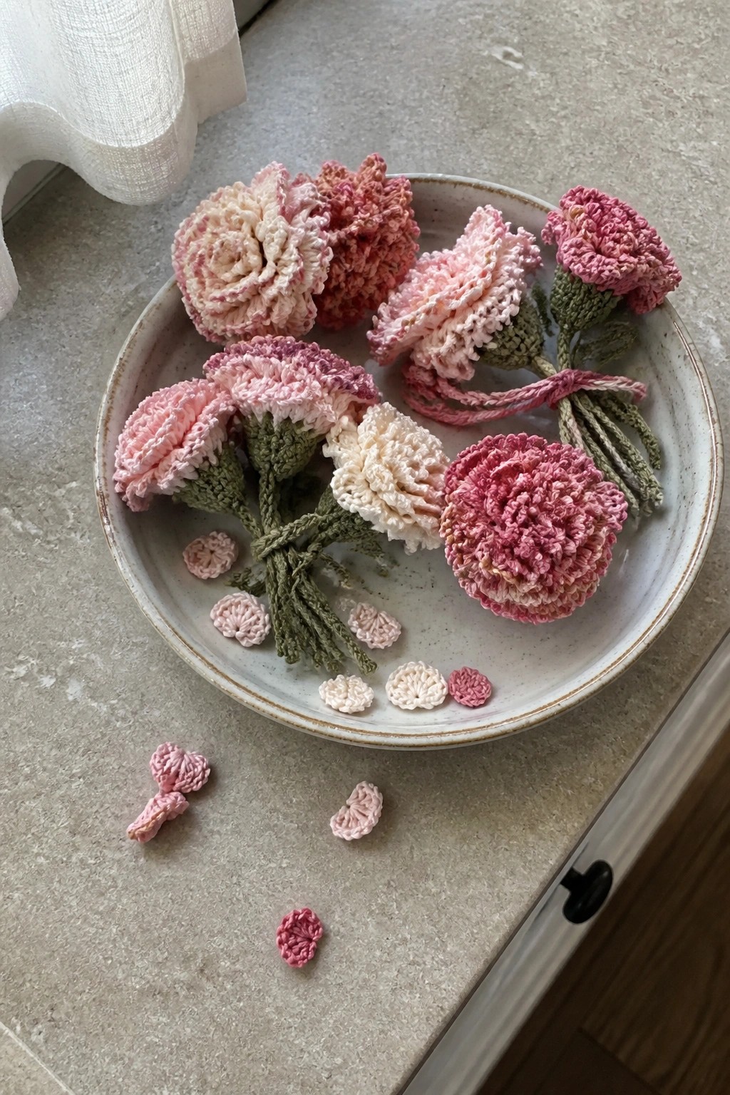Pink crocheted flowers bundled on a ceramic plate with scattered loose pieces.