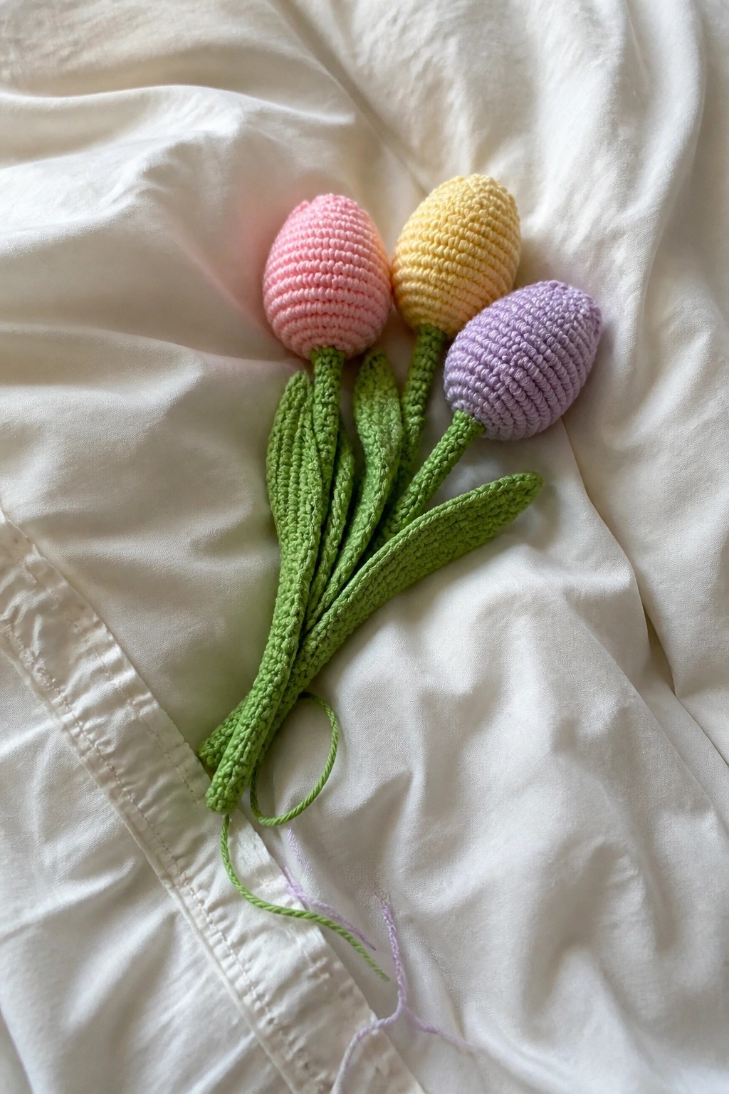 Three crocheted tulips in pink, yellow, and purple on white fabric.