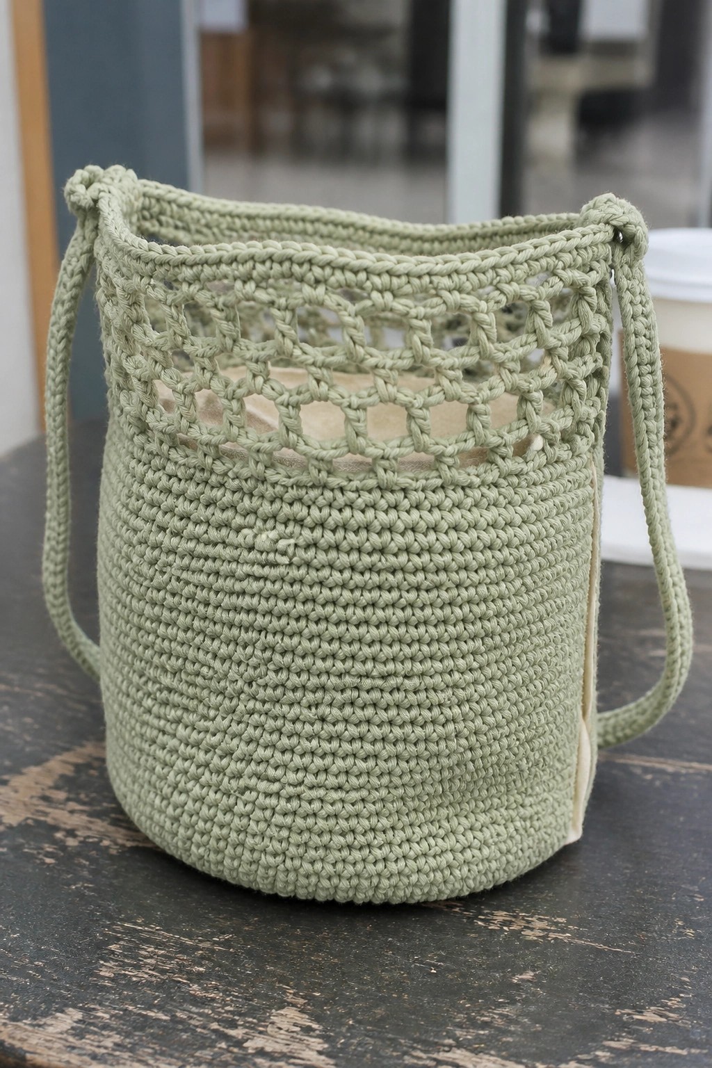 Sage green crocheted bucket bag with open lace top on wooden table