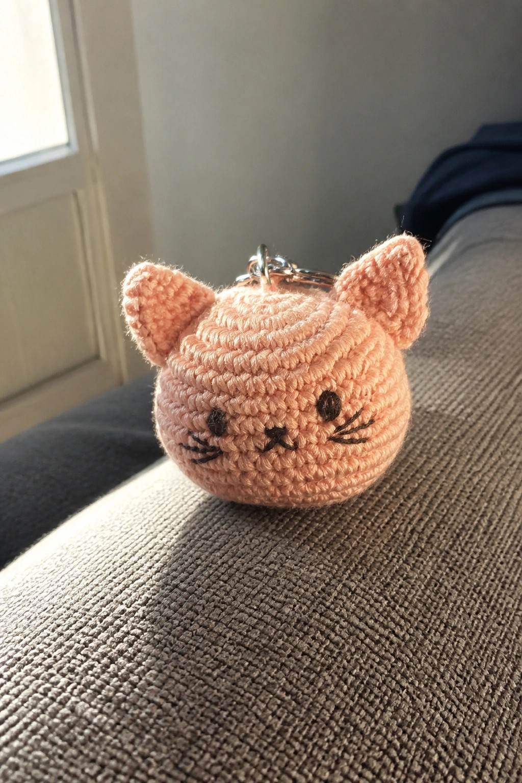 Peach crocheted cat keychain with embroidered face on gray fabric surface