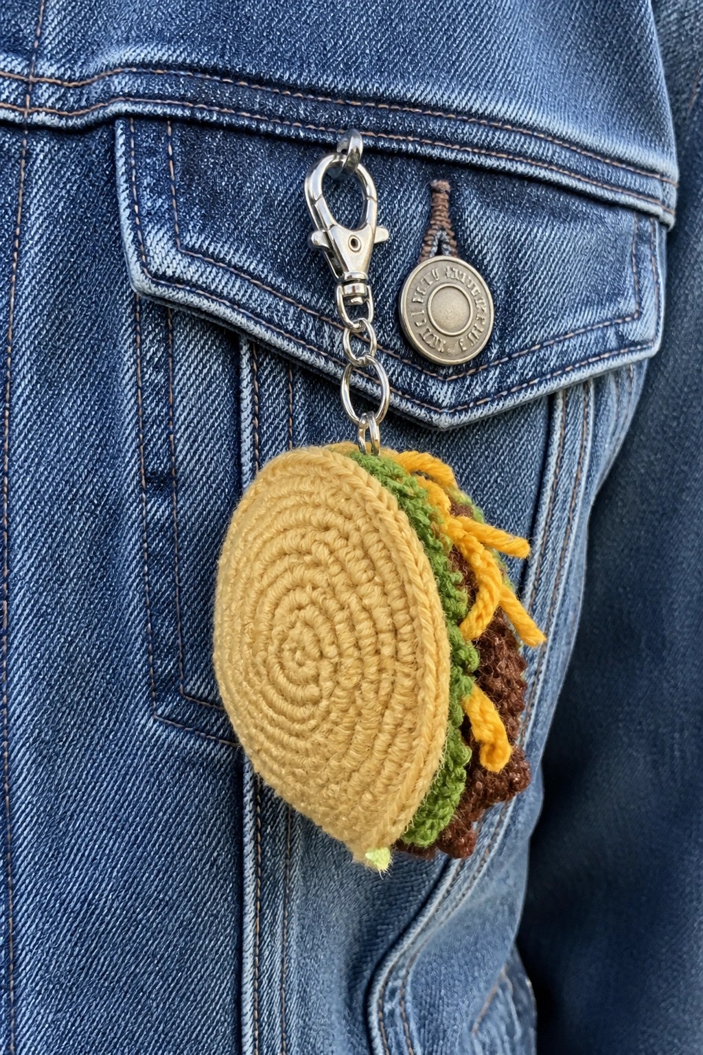 Crocheted hamburger keychain clipped to pocket of blue denim jacket.