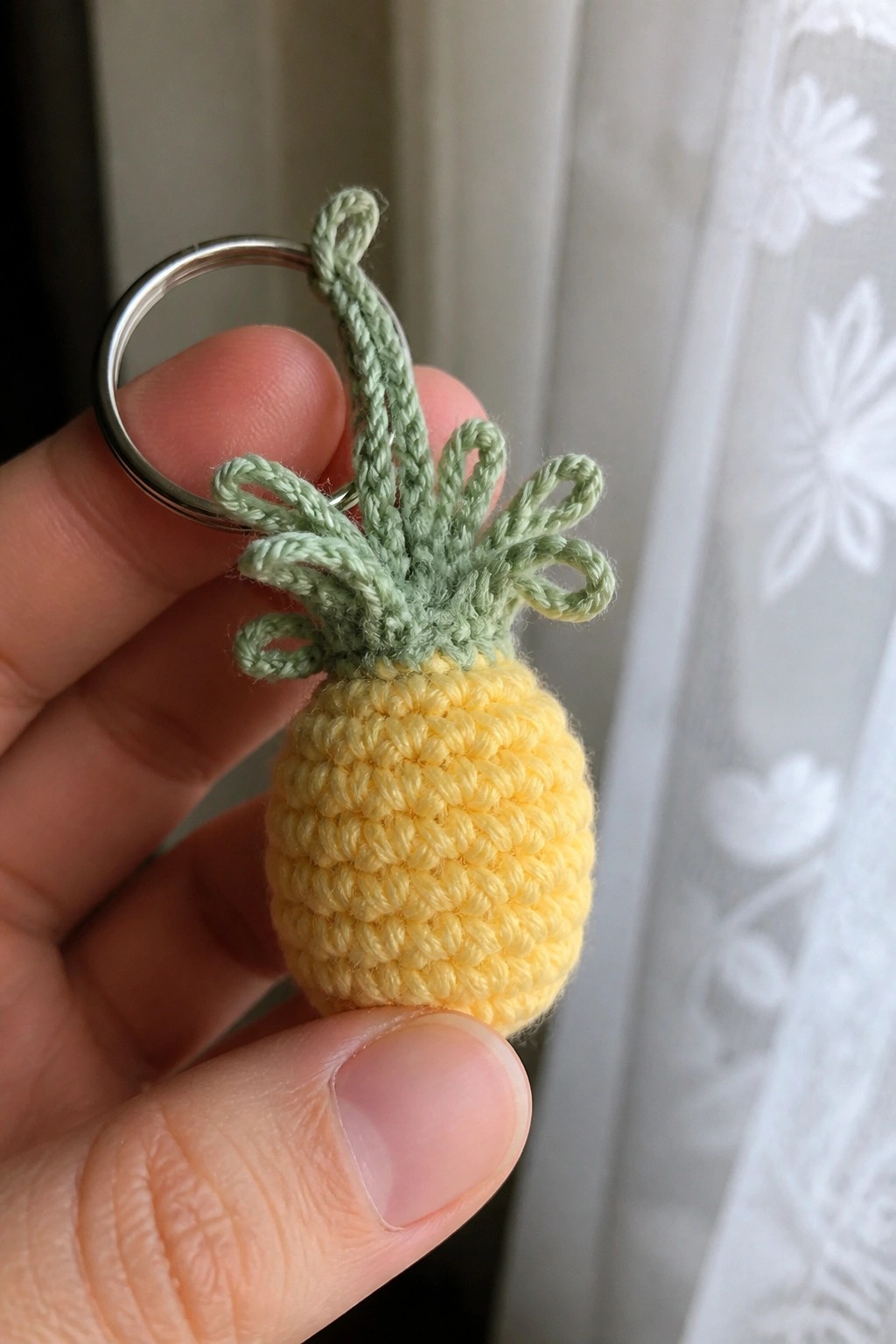 Hand holding yellow crocheted pineapple keychain with green top and metal ring