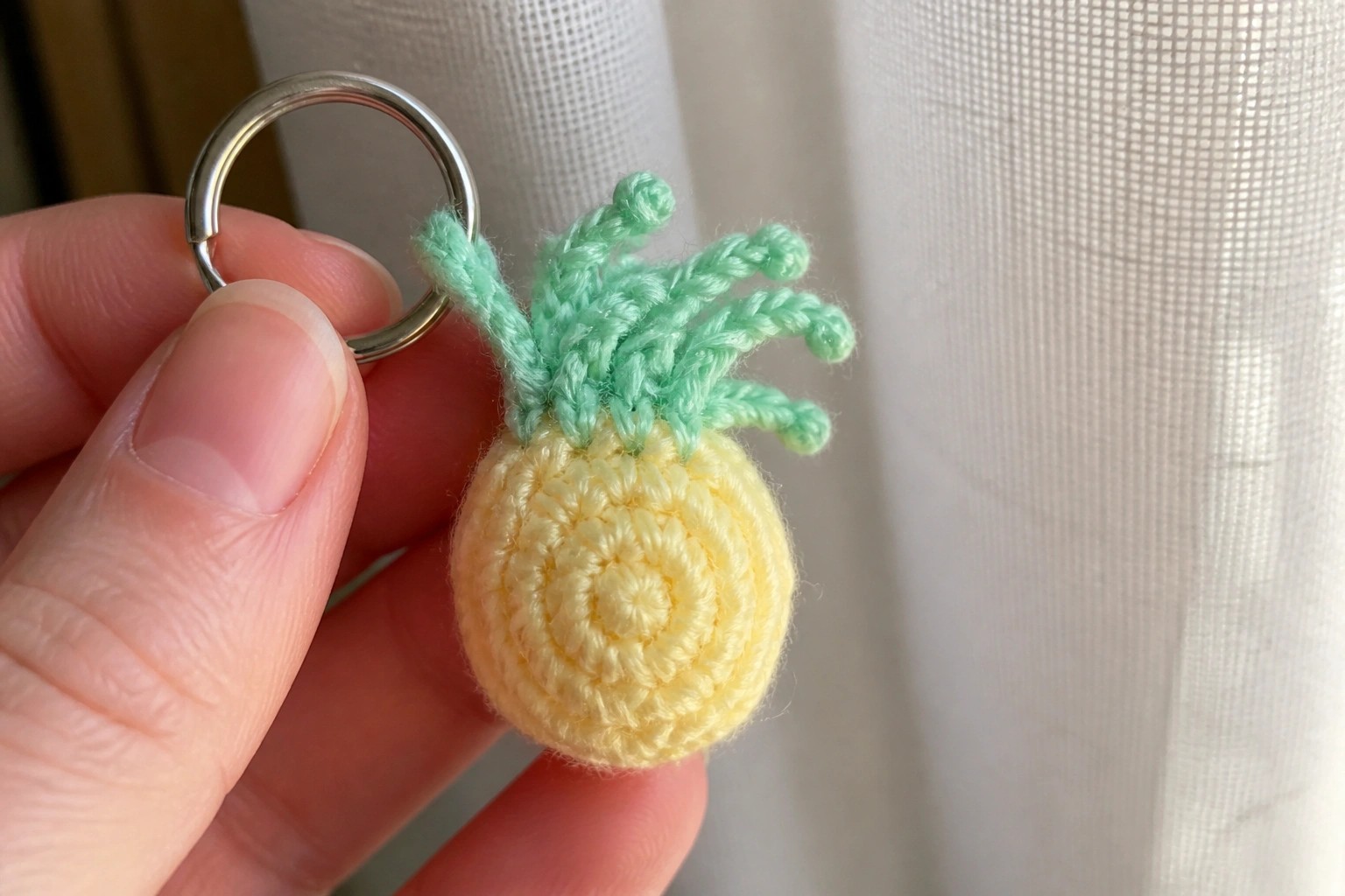 Hand holding yellow crocheted pineapple keychain with green top and metal ring