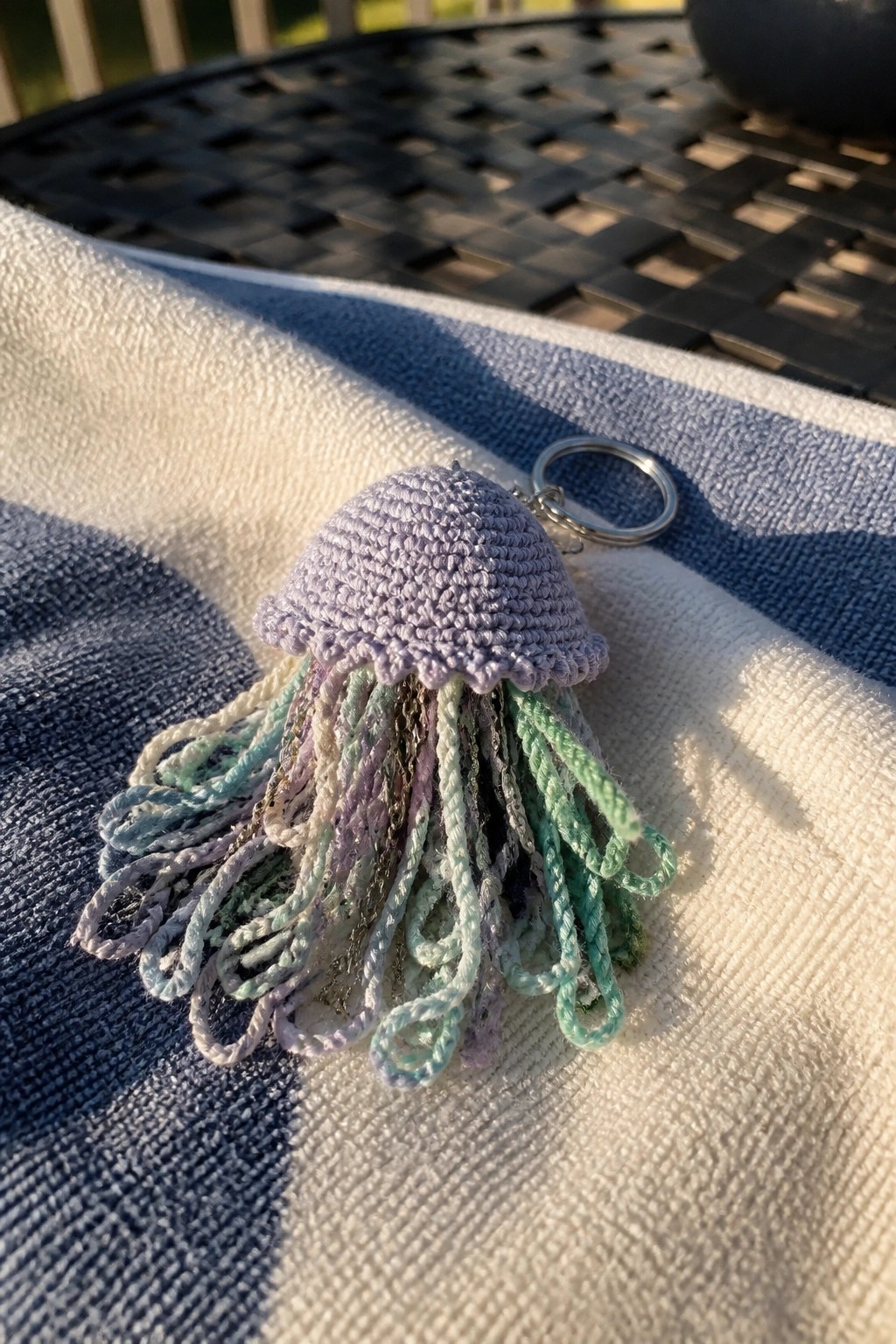 Crocheted lavender jellyfish keychain with pastel tentacles on blue striped towel