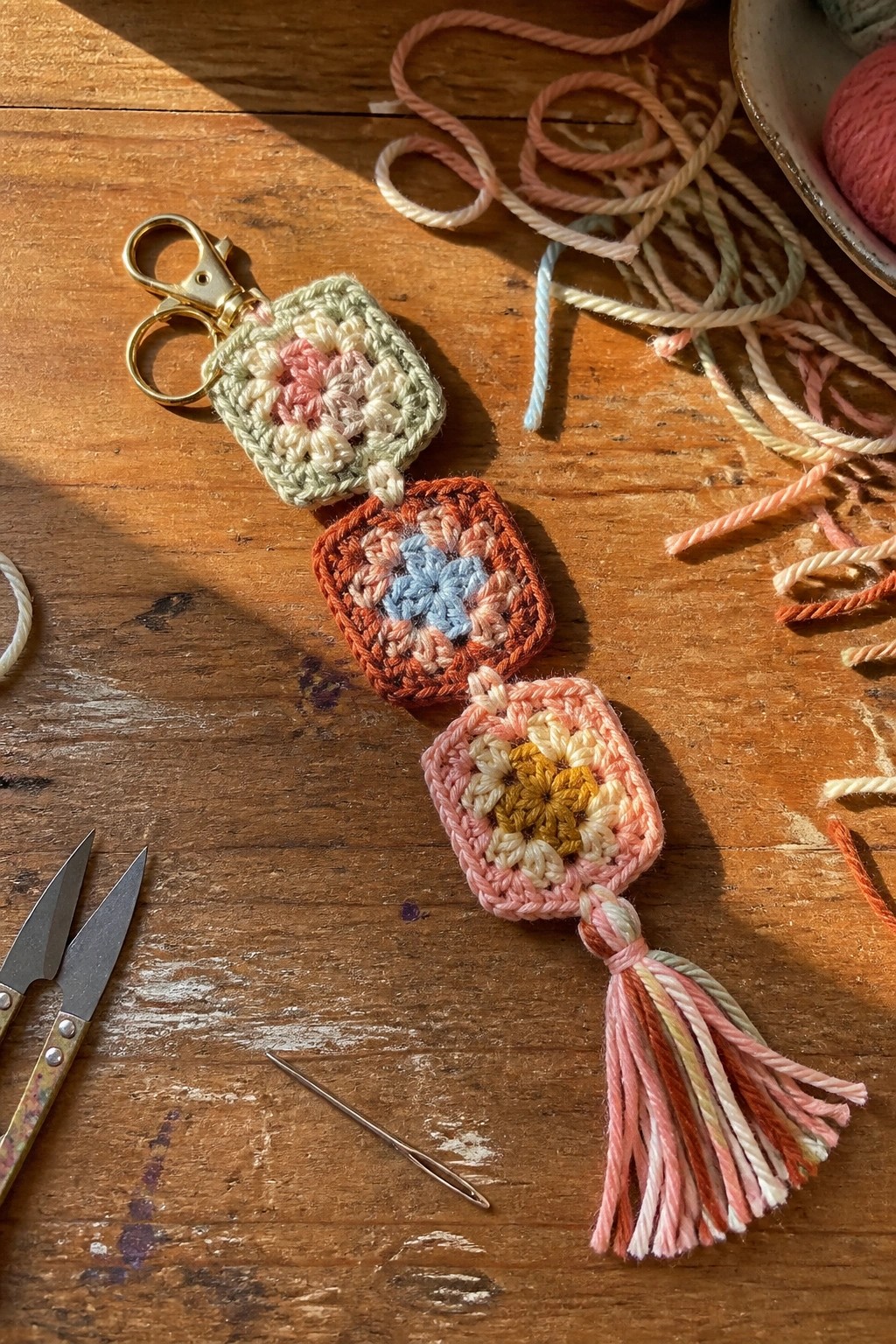 Pastel crocheted granny squares keychain with gold clasp and tassel on wood