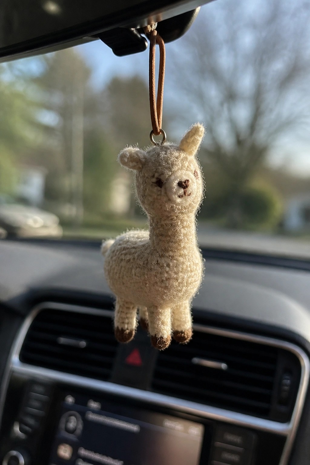 Crocheted cream llama ornament hanging from car rearview mirror above dashboard