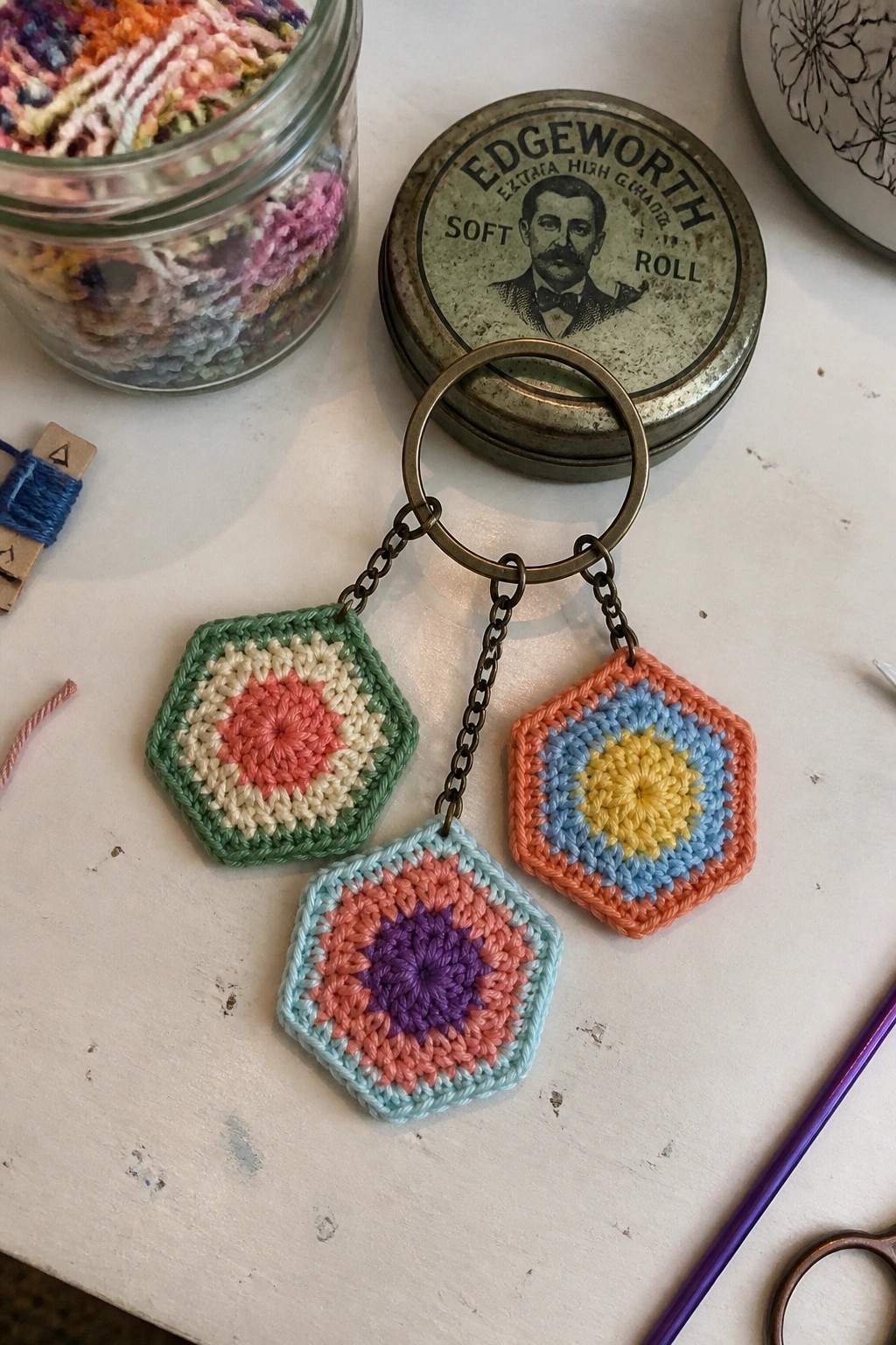 Three small crocheted hexagonal motifs in different color combinations hang from chains on a metal keyring.