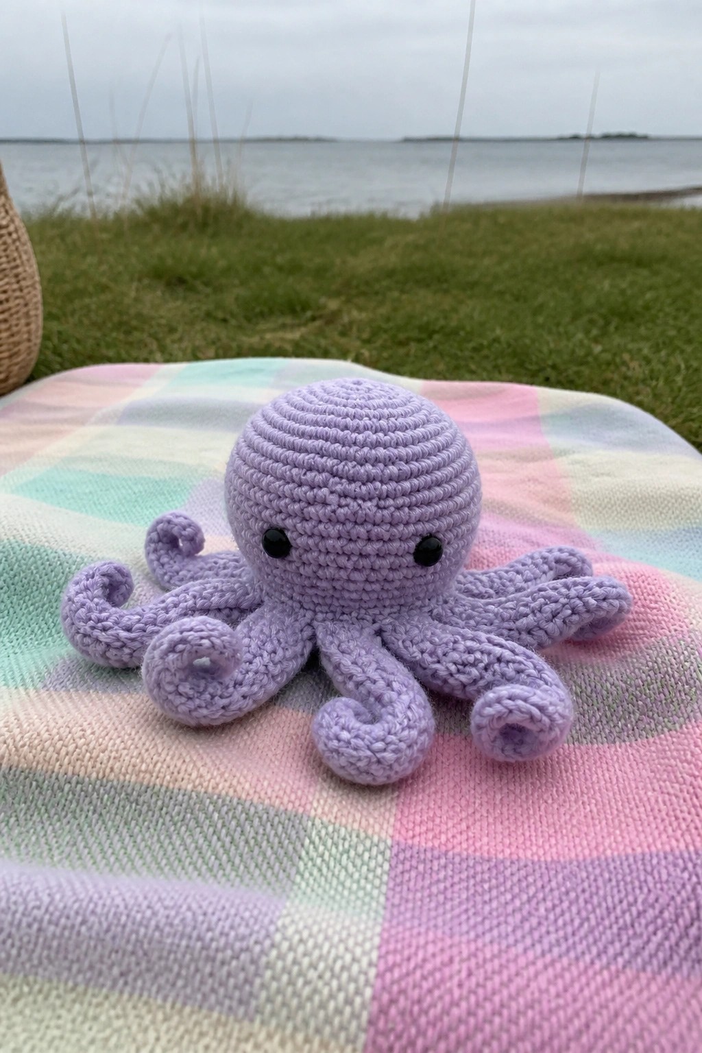Purple crocheted octopus on pastel plaid blanket by the water.