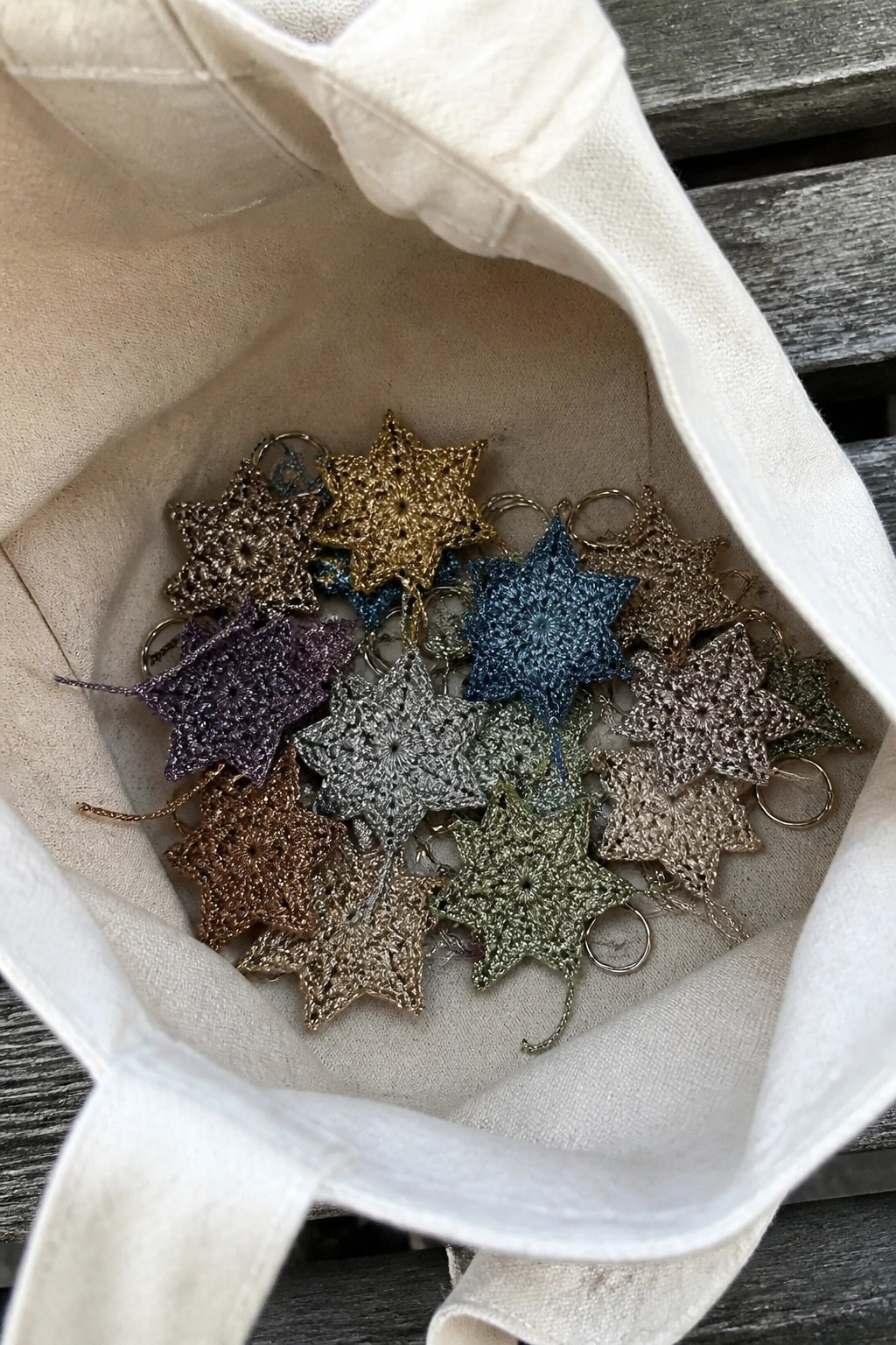 Multiple crocheted star keychains in assorted metallic colors piled inside a white tote bag.