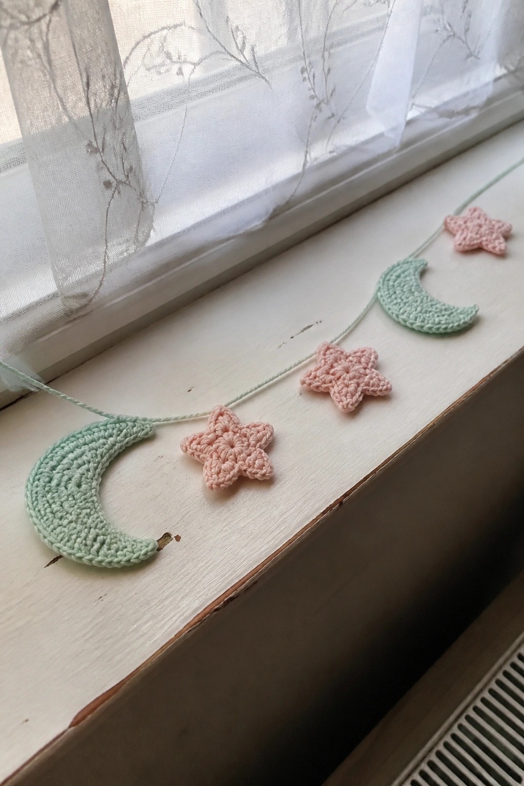 Pastel crocheted moons and stars garland on white windowsill