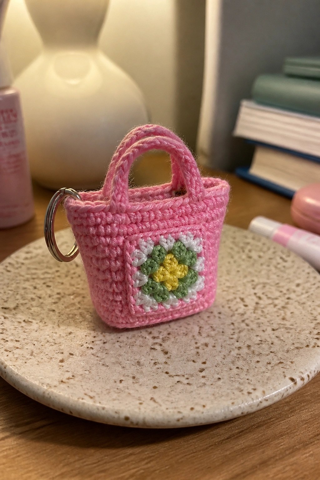 Pink crocheted mini handbag keychain with floral granny square on speckled plate