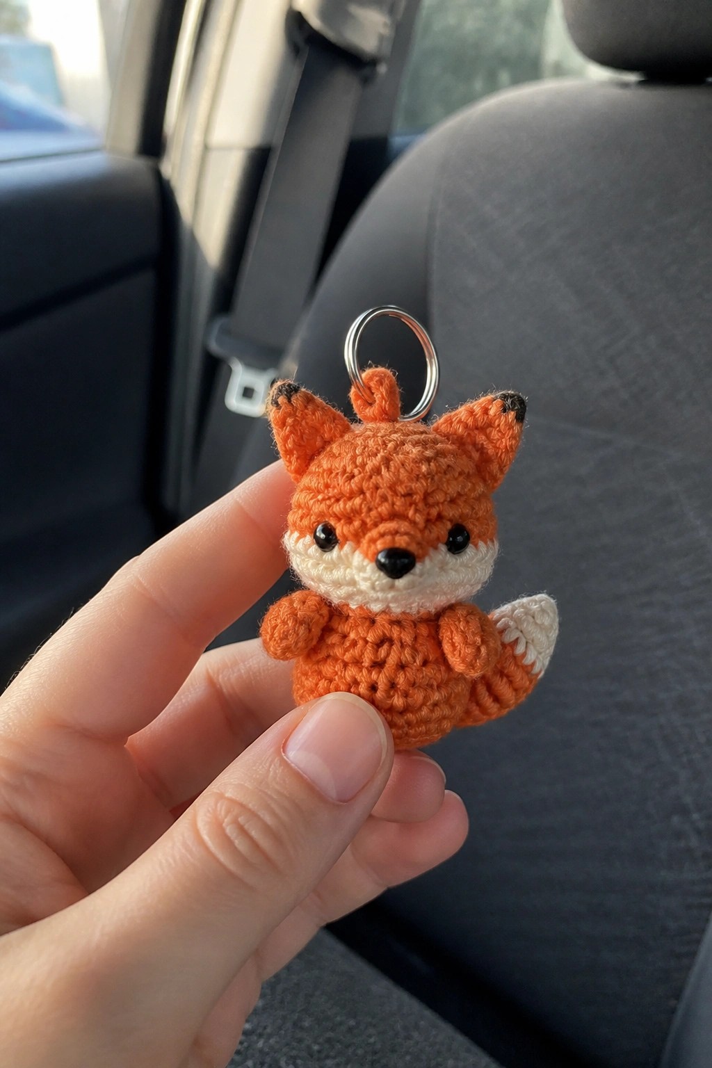 Hand holding a crocheted orange fox keychain with metal ring in a car