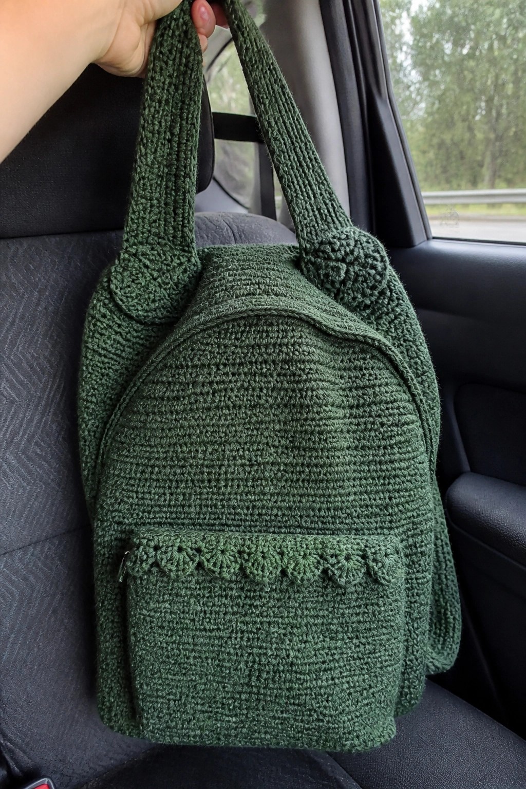 Green crocheted backpack with front pocket held by hand in car