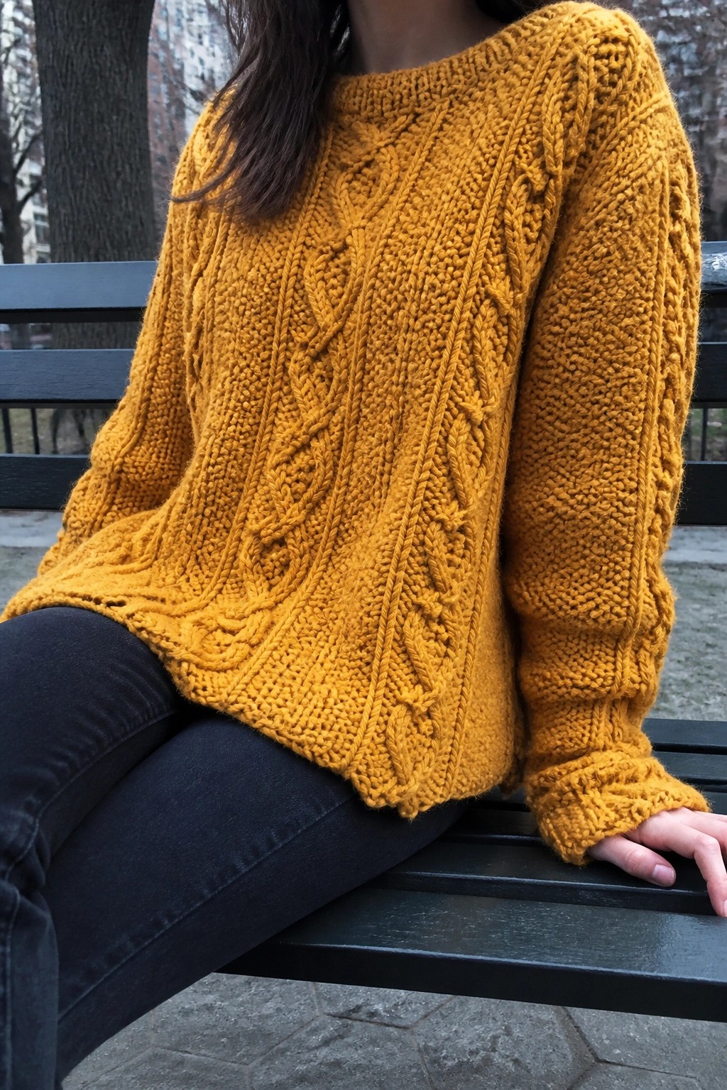 Woman in chunky mustard cable-knit sweater seated on dark park bench