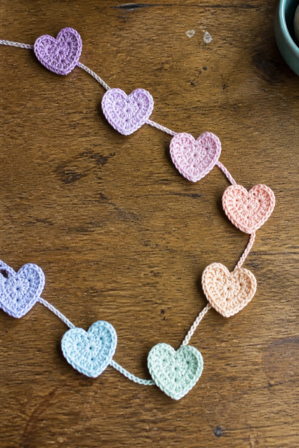 Pastel crocheted hearts strung as garland on rustic wooden table