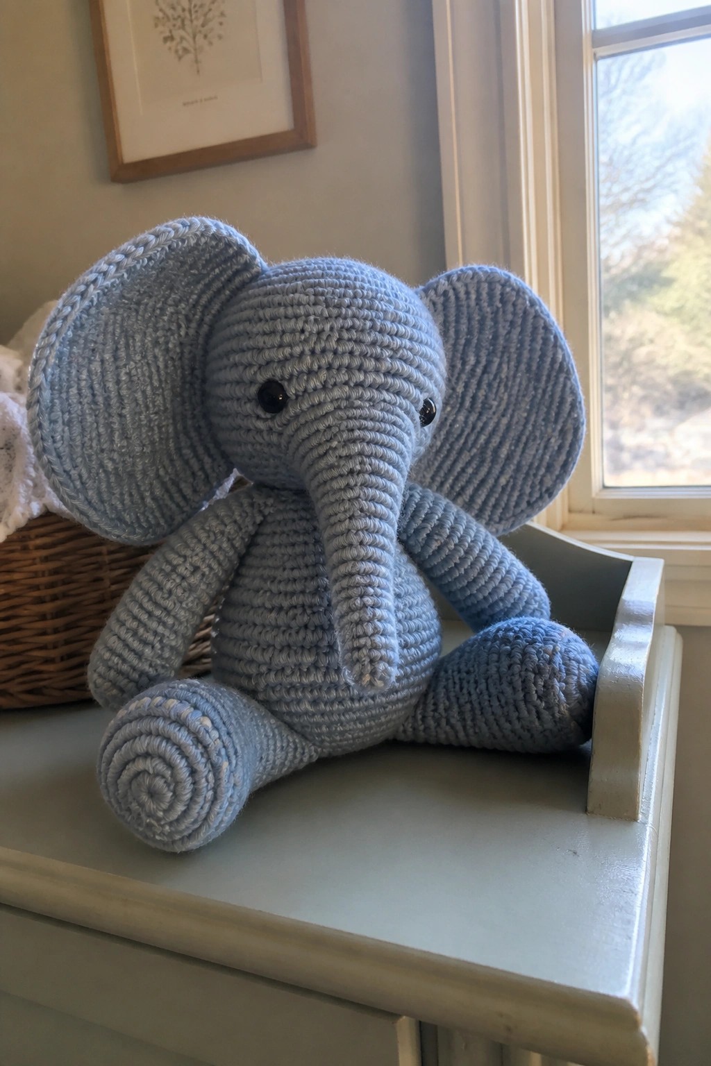 Light blue crocheted elephant toy with large ears on a windowsill.