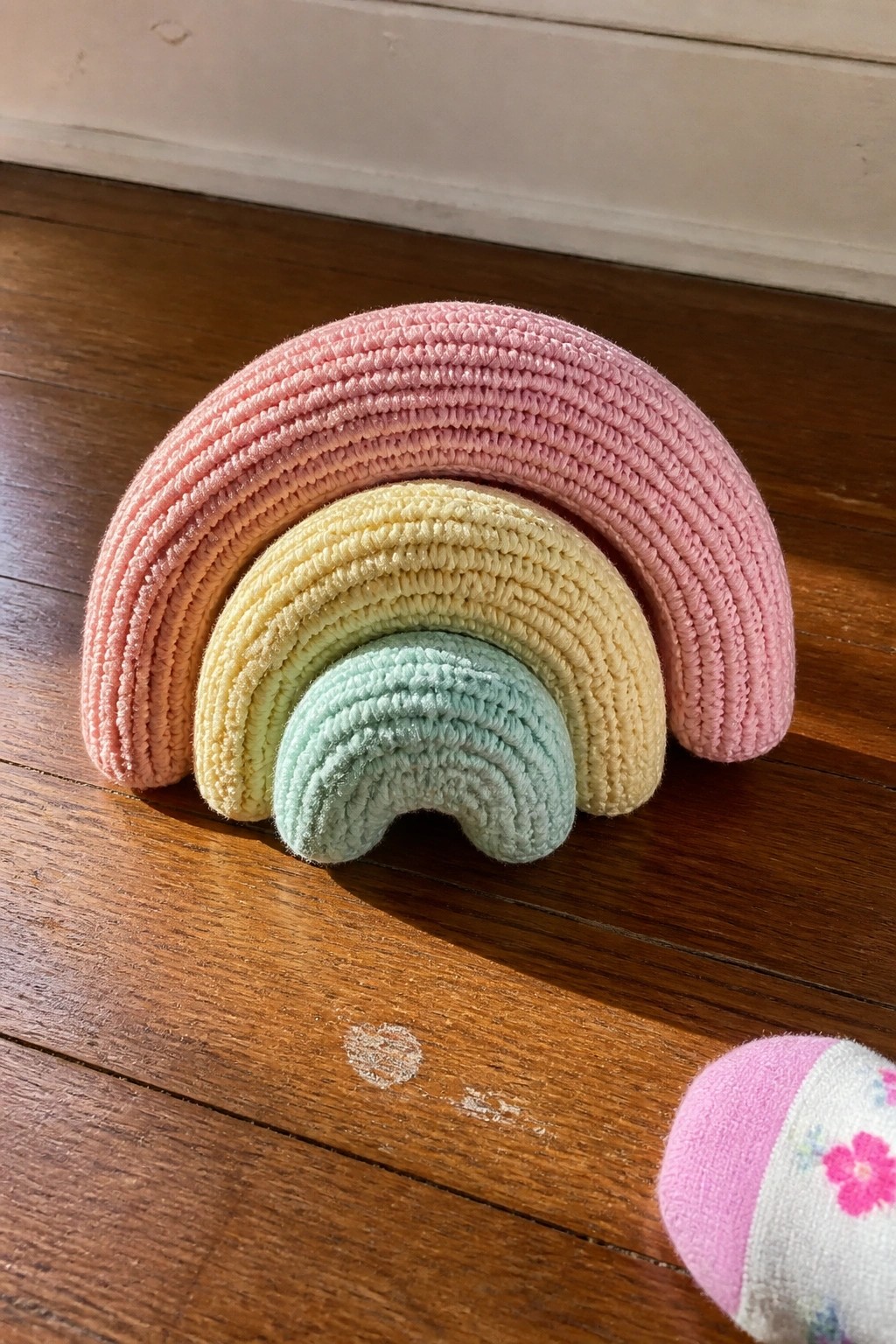 Crocheted rainbow toy with pink, orange, yellow, and mint arches on wooden floor