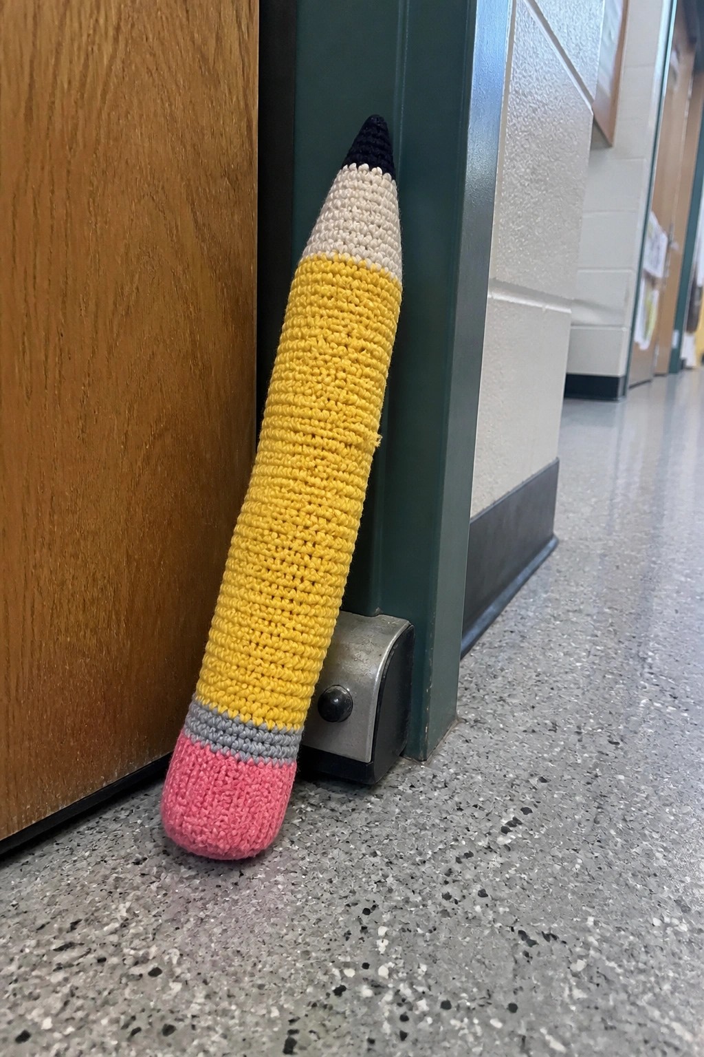 Crocheted yellow pencil doorstop with pink eraser propping open green door