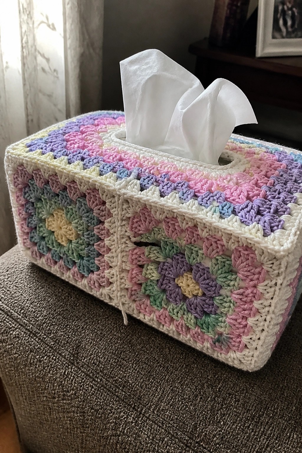 Pastel crocheted granny square tissue box cover with white tissues on brown fabric