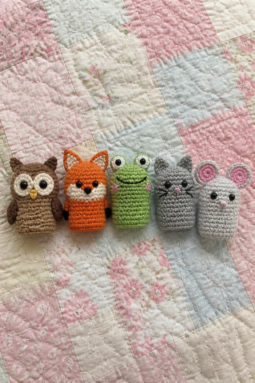 Five small crocheted animal finger puppets lined up on a quilt.