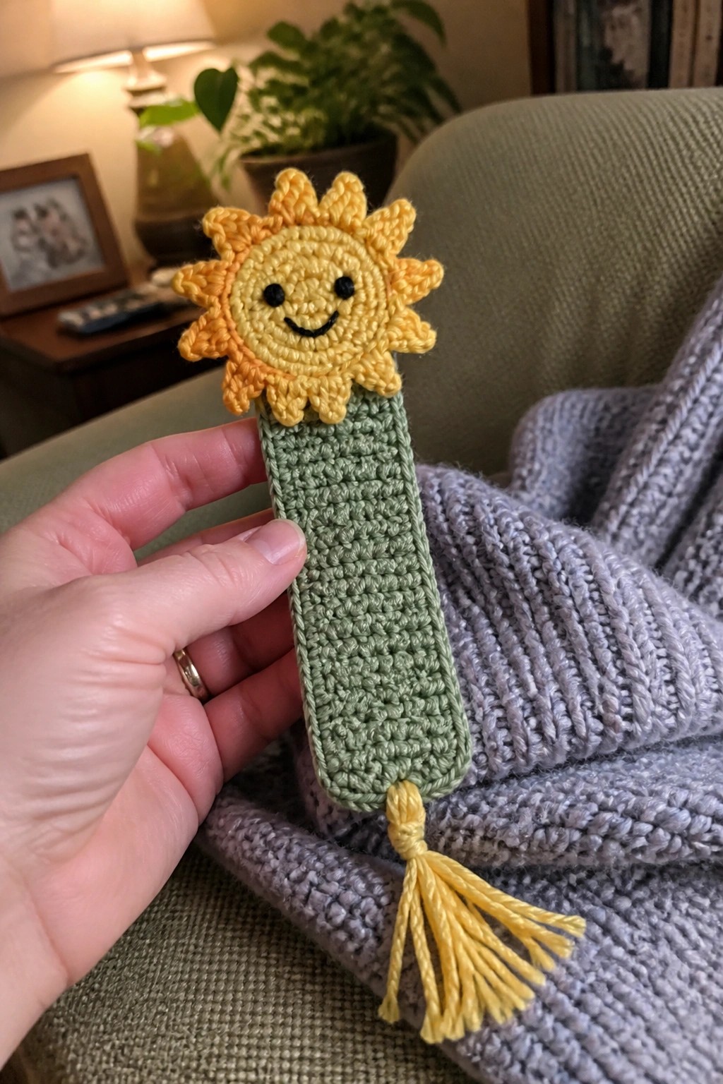 Hand holding crocheted smiling sun bookmark with green body and yellow tassel
