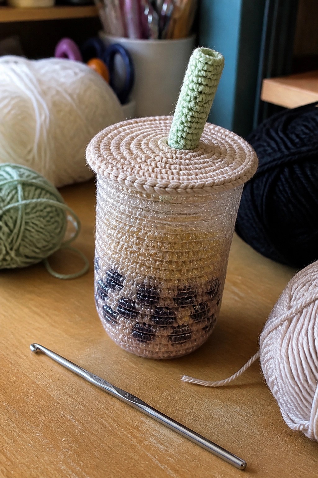 Crocheted bubble tea cup with brown boba section, green straw, yarn balls, and hook