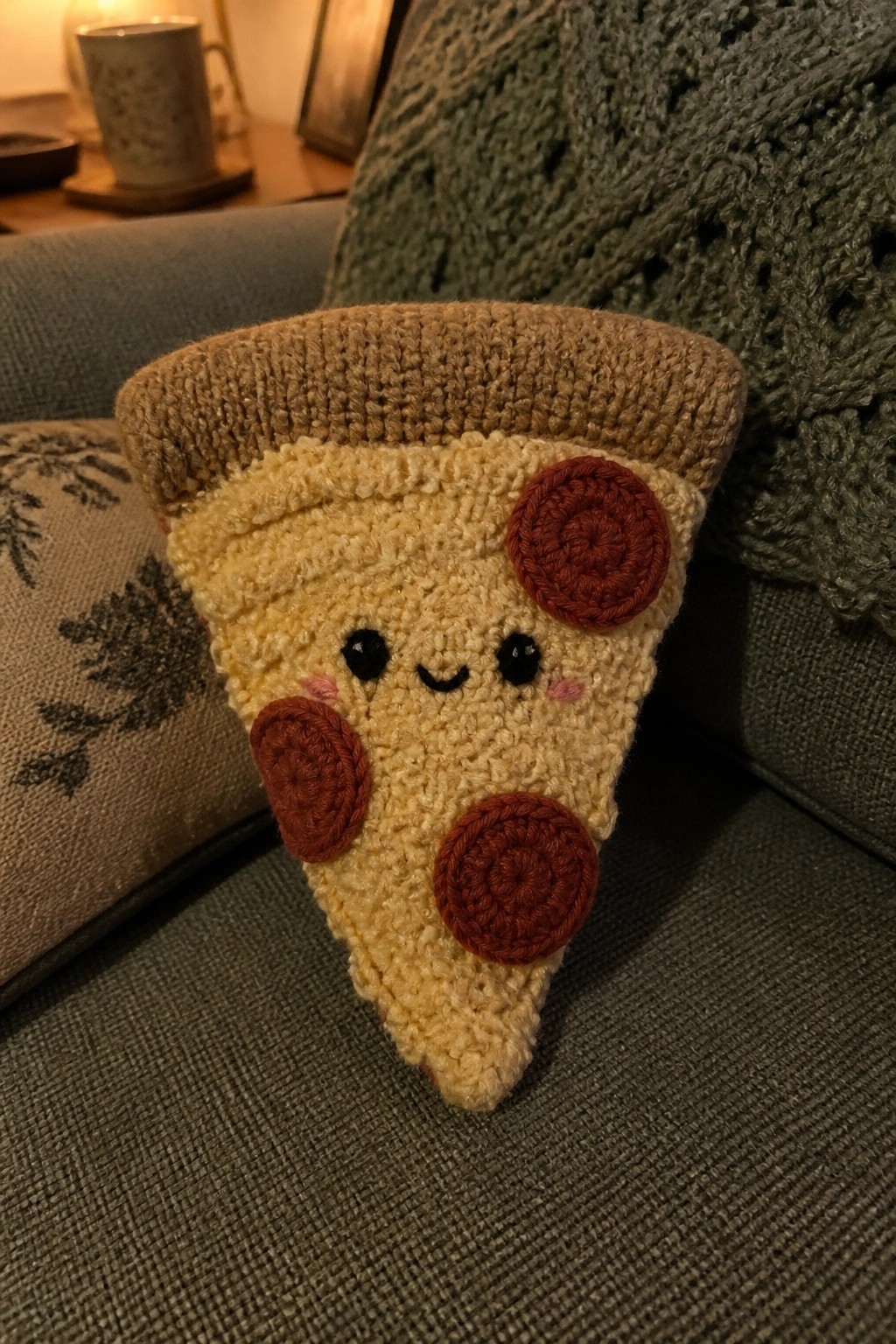 Crocheted pizza slice toy with cute face and pepperoni on couch