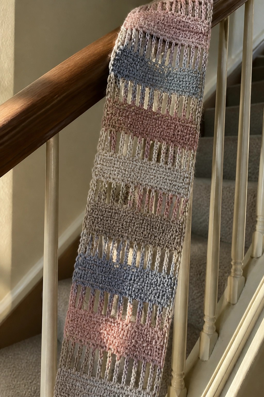 Pastel striped crocheted scarf with mesh pattern draped over wooden stair banister
