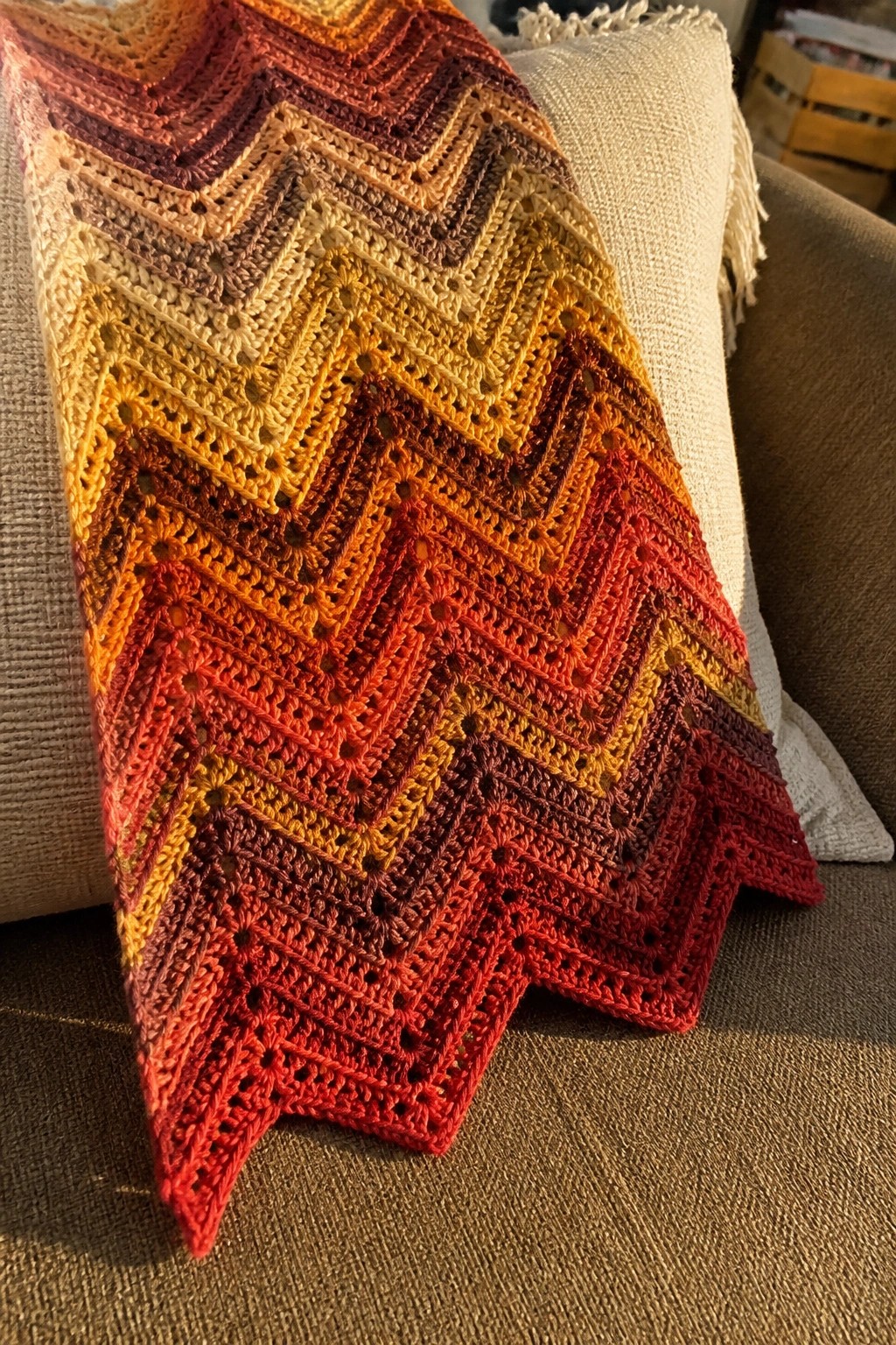 Crocheted chevron blanket in autumn colors draped over a couch with pillows.