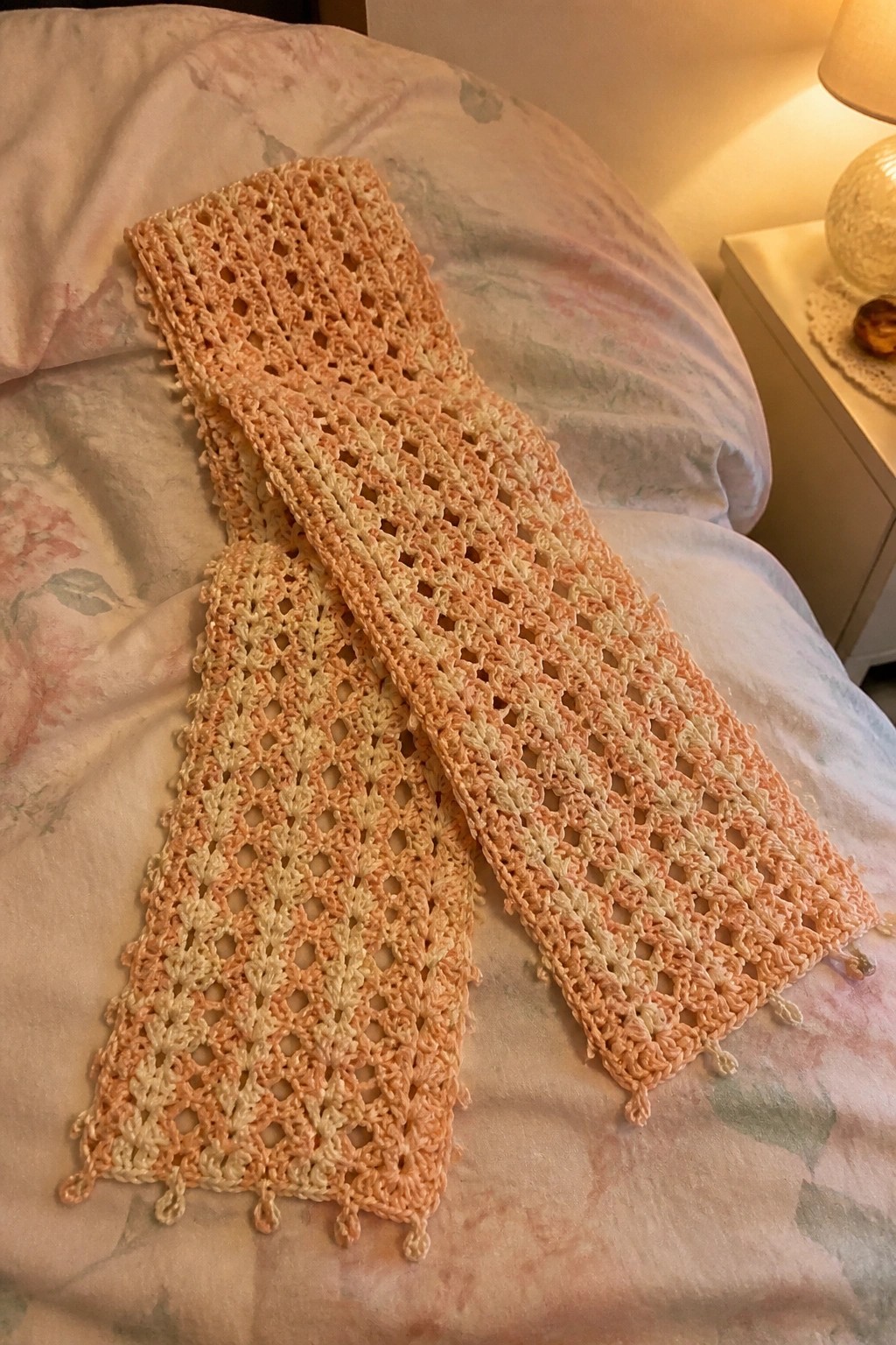 Peach ombre crocheted lace scarf with tassels on floral bedspread