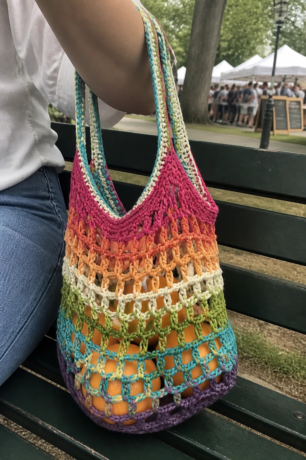 Rainbow crocheted mesh bag of oranges on bench in park
