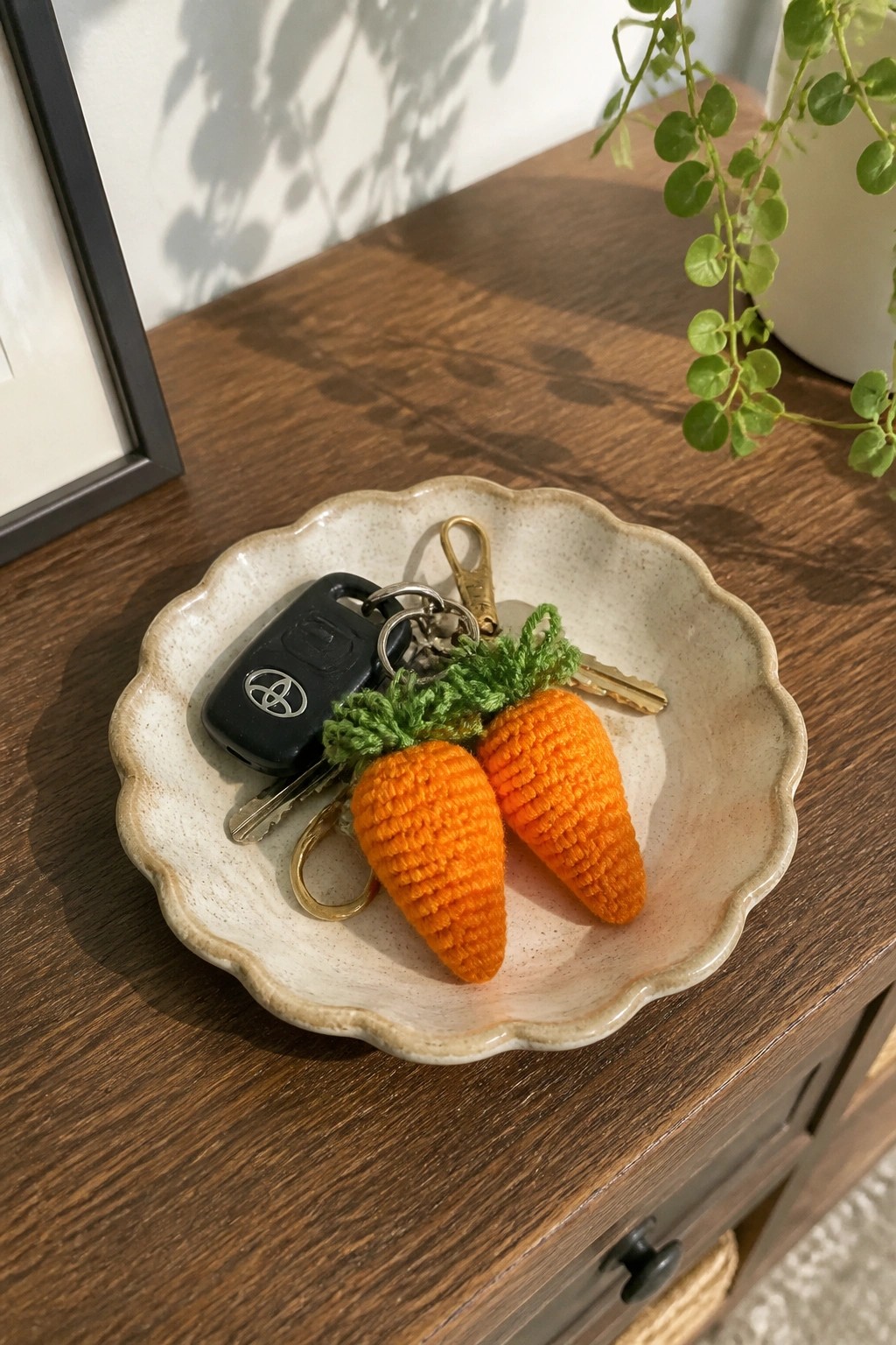 Crocheted orange carrot keychains and Toyota keys in a scalloped ceramic bowl on wood.