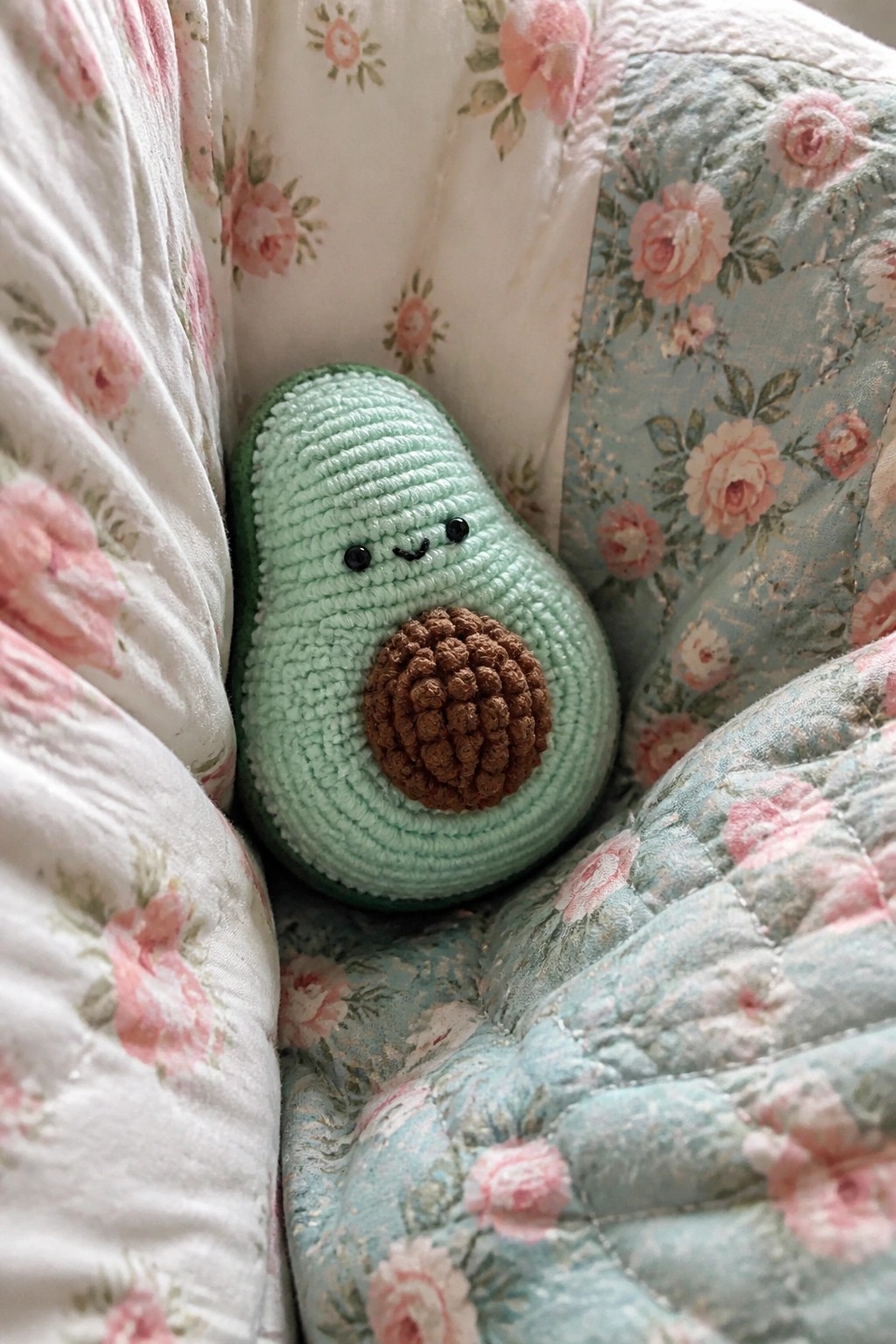 Crocheted avocado plush with smiling face nestled in floral quilts