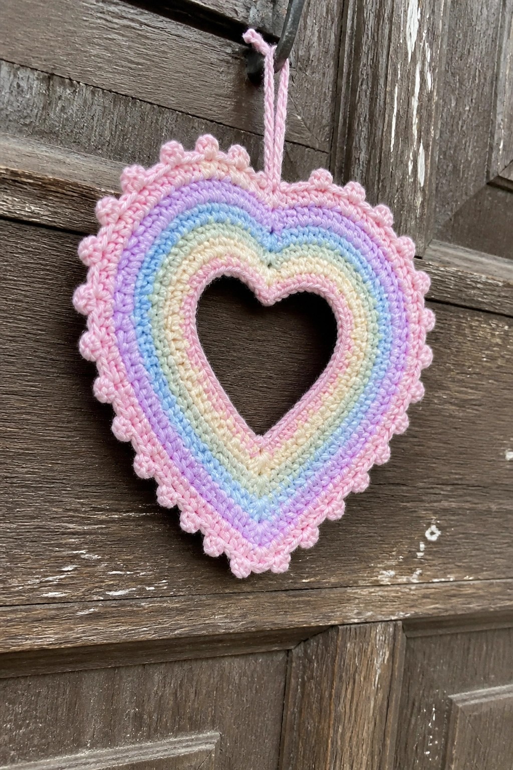 Rainbow crocheted heart with pink scalloped border hanging on wooden door