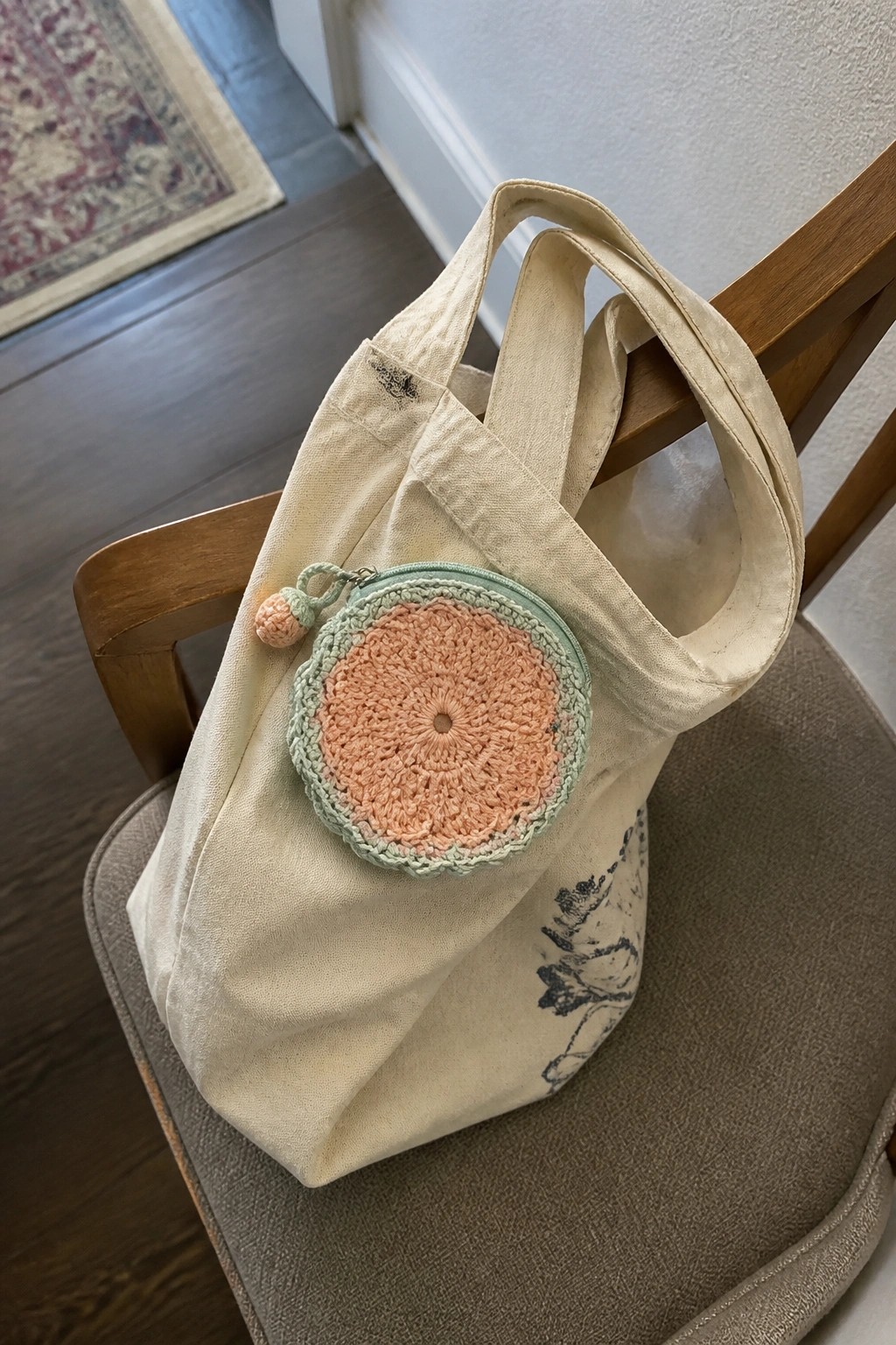 Canvas tote bag with a round crocheted pouch in peach and mint attached to the front.