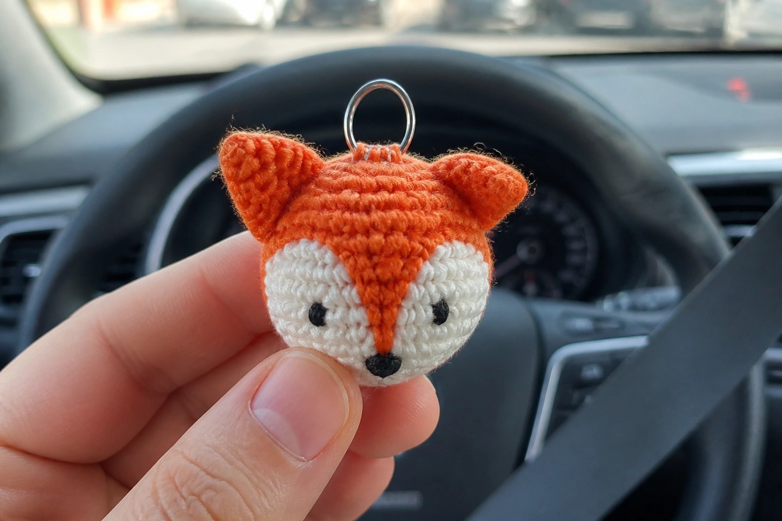 Hand holding orange crocheted fox keychain with white face and metal ring in car