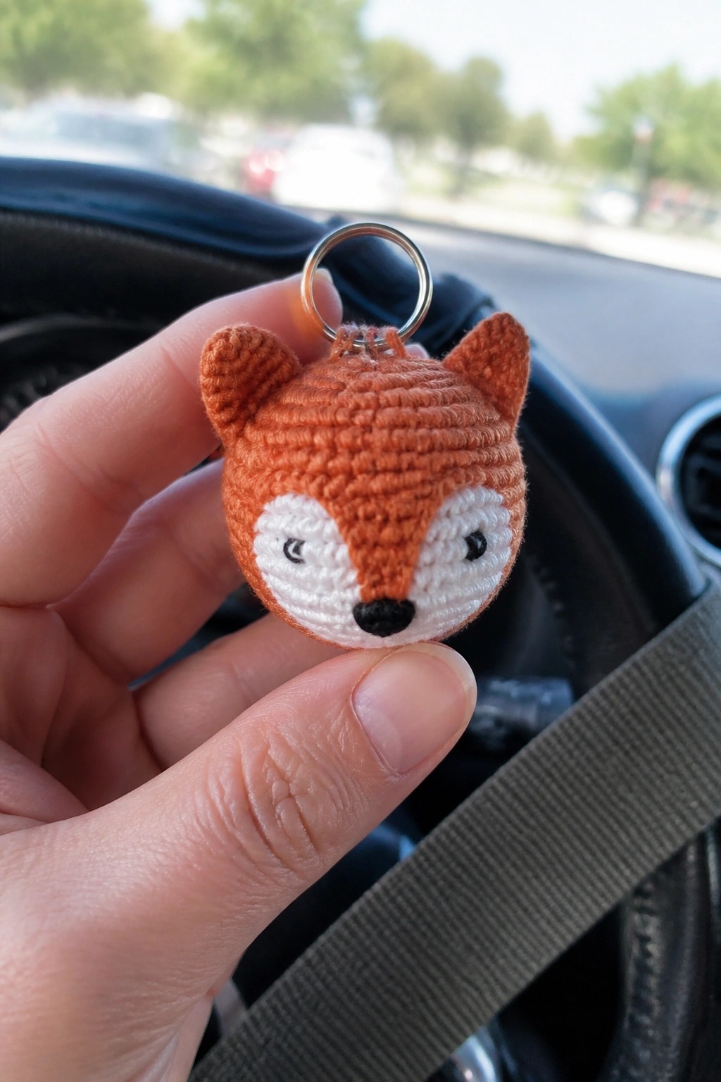 Hand holding orange crocheted fox keychain with white face and metal ring in car