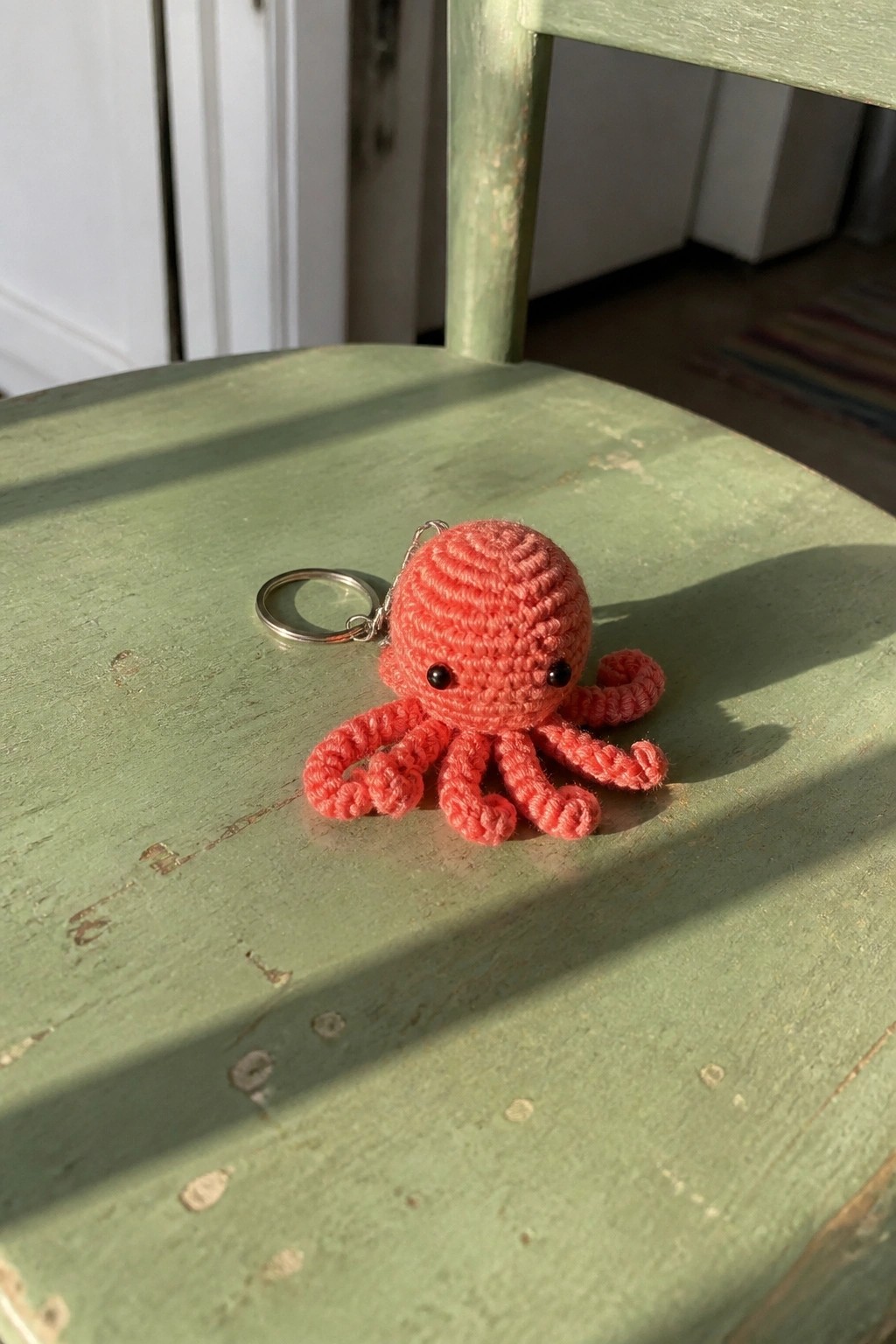 Pink crocheted octopus keychain with black eyes on green wooden chair.