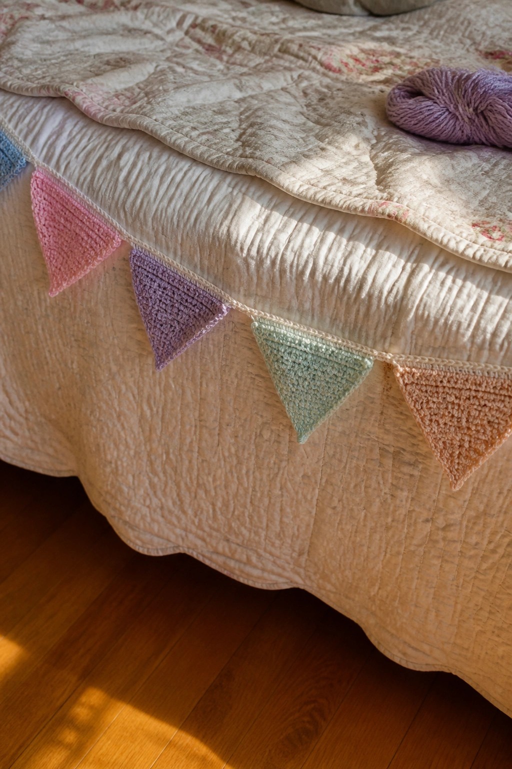 Crocheted colorful bunting draped over a quilt with purple yarn nearby