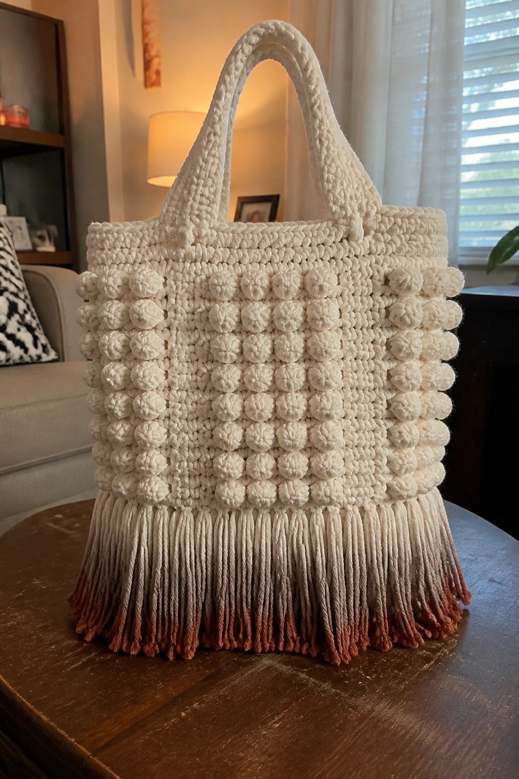 White crocheted tote bag with bobble texture and ombre brown fringed bottom on table