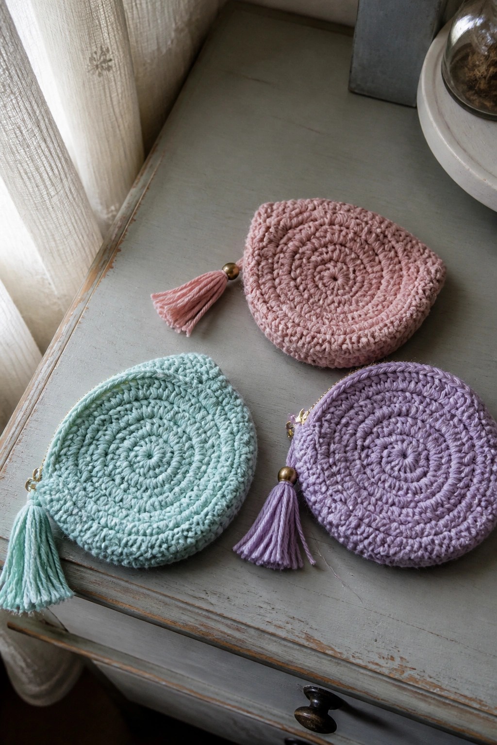 Three crocheted round coin purses in pink, mint, and purple with tassels