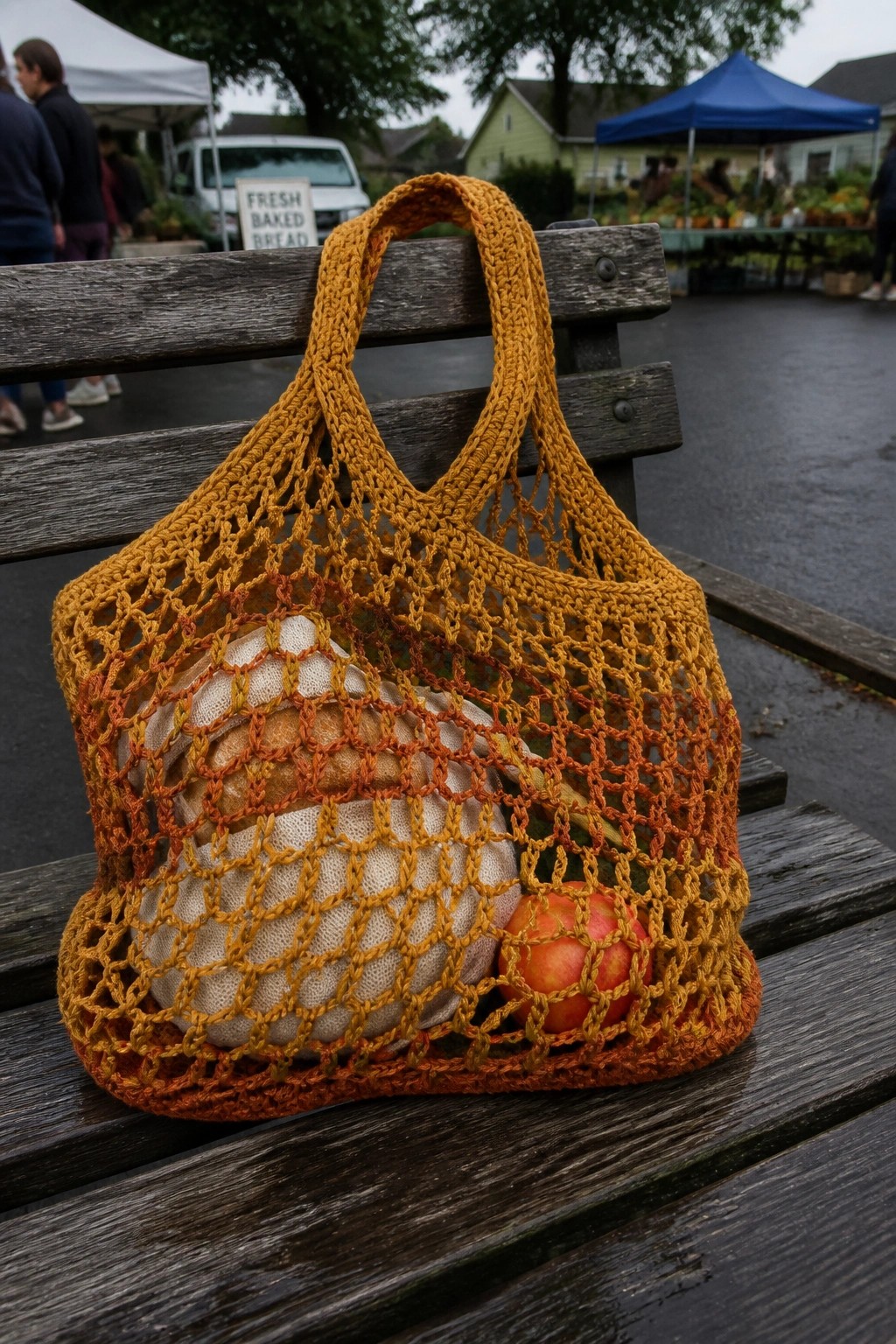 Yellow-orange crocheted net bag with bread and apple on wooden bench