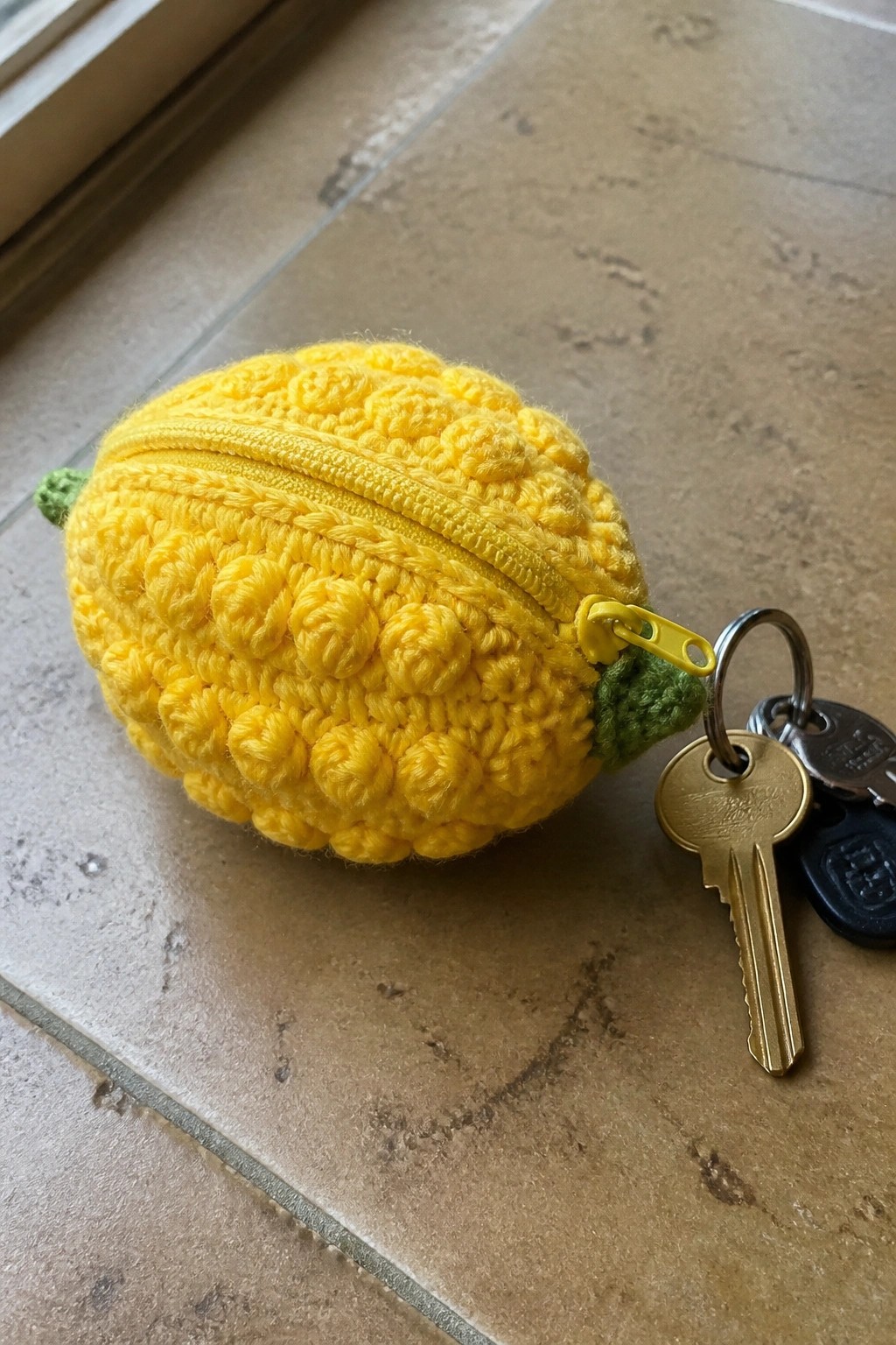 Yellow crocheted lemon pouch with zipper and attached keys on tiles