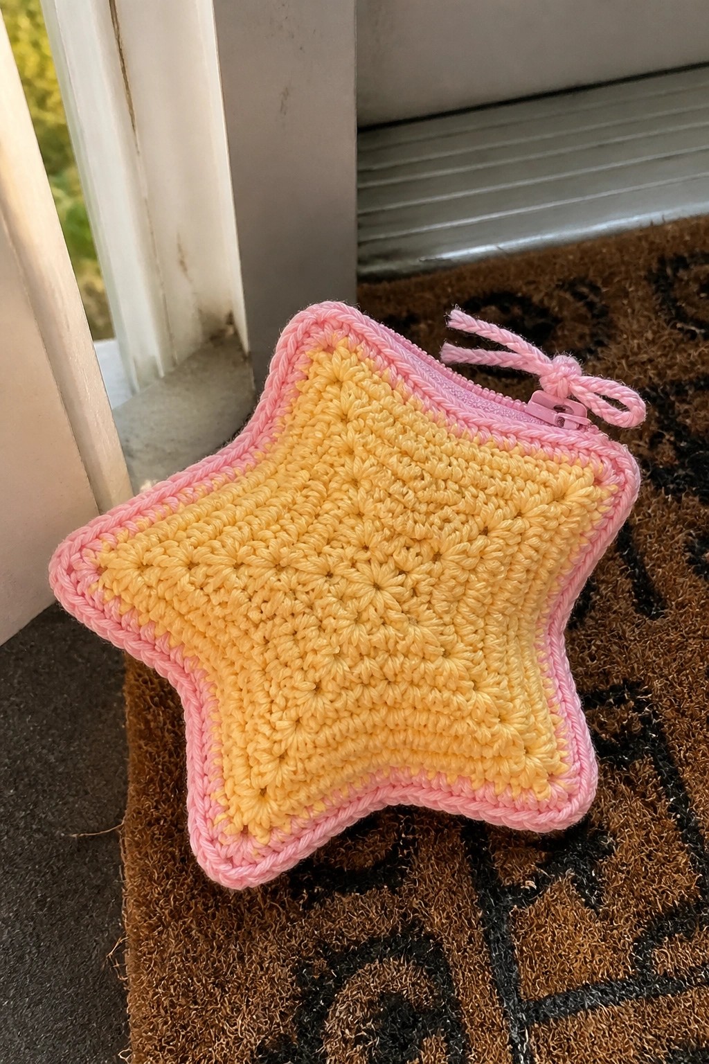 Yellow crocheted star pouch with pink zipper and border on brown doormat