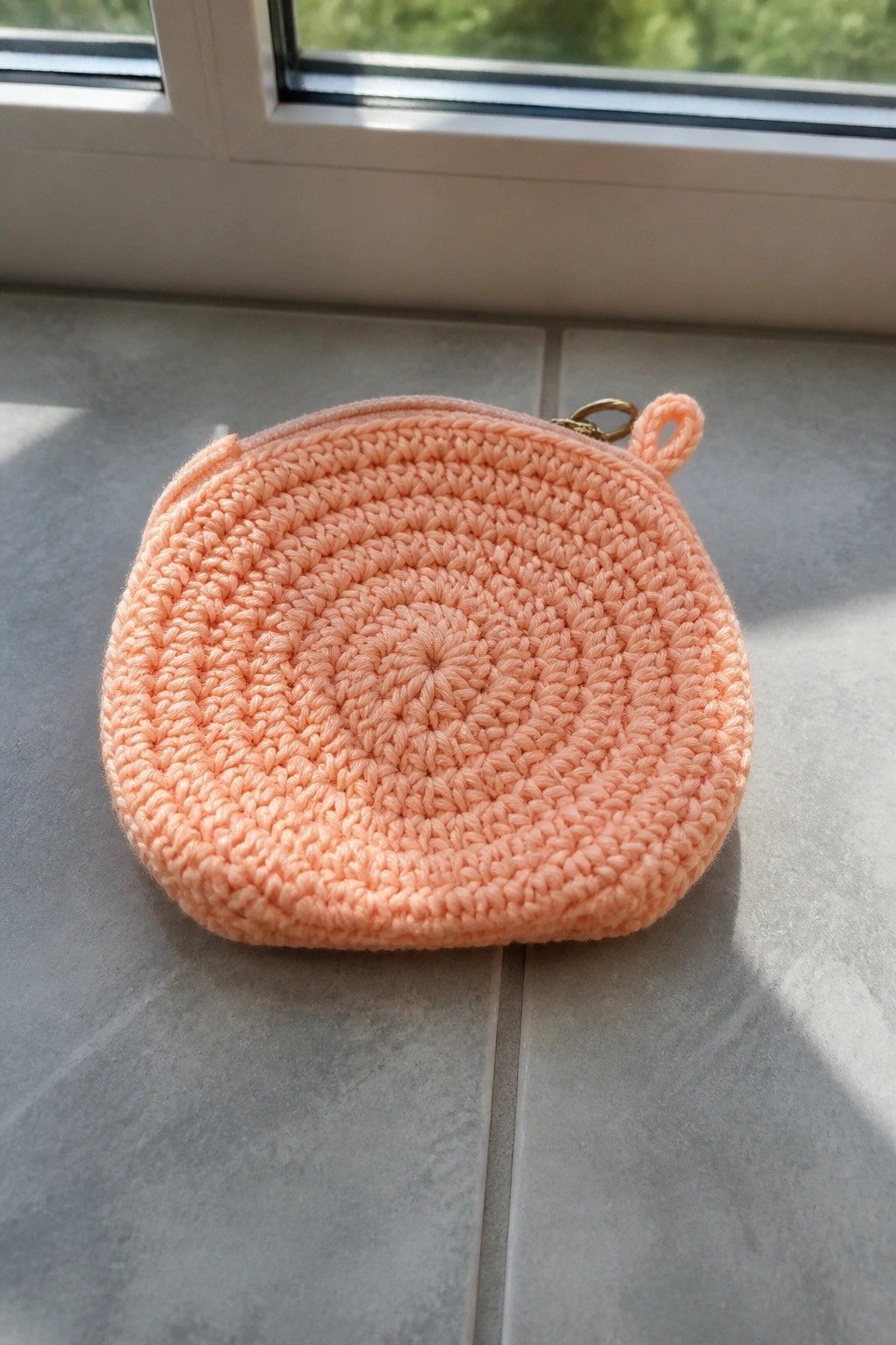 Peach crocheted round pouch with zipper on gray tiled windowsill ledge